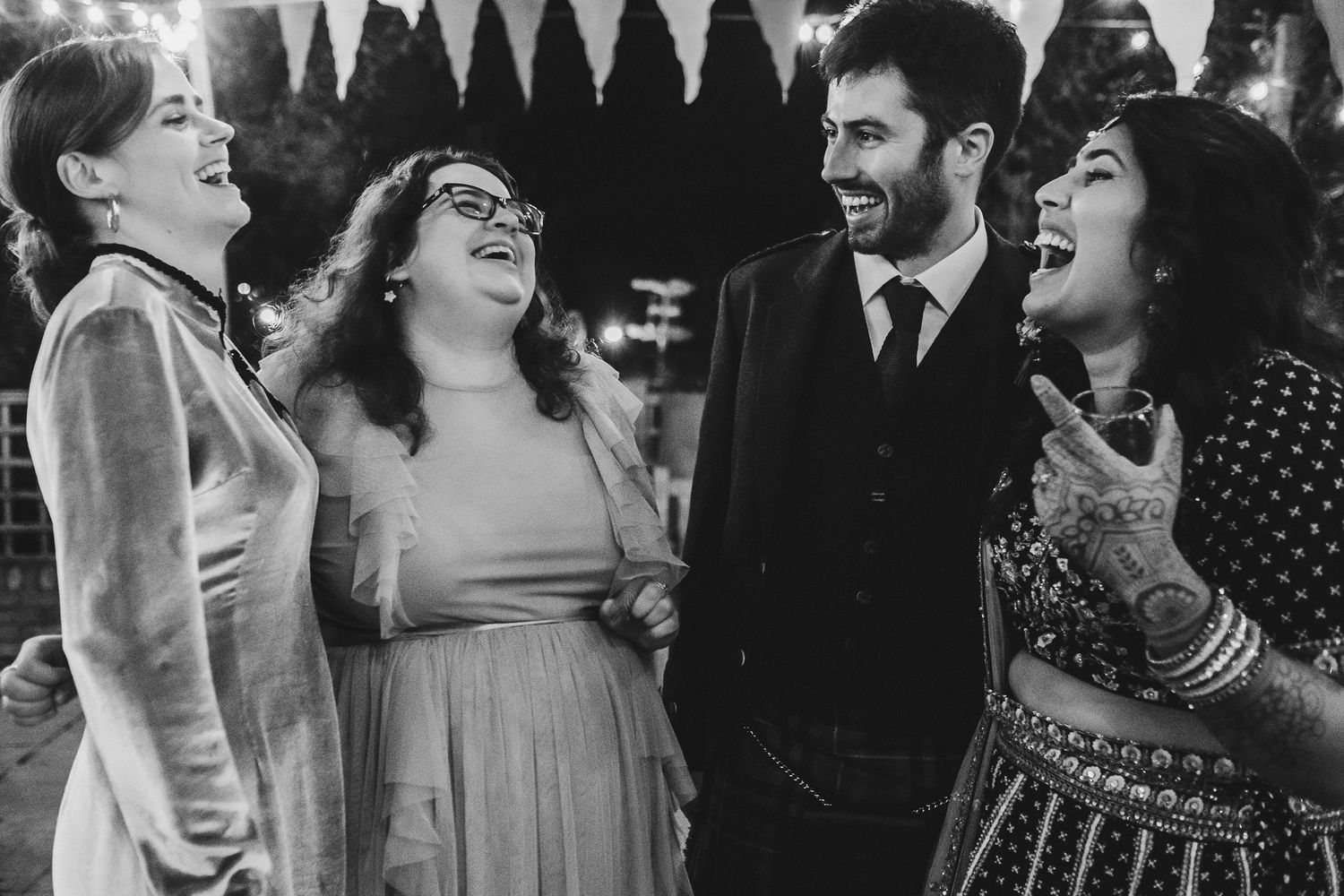 A group of wedding guests share a candid moment of laughter in black and white.