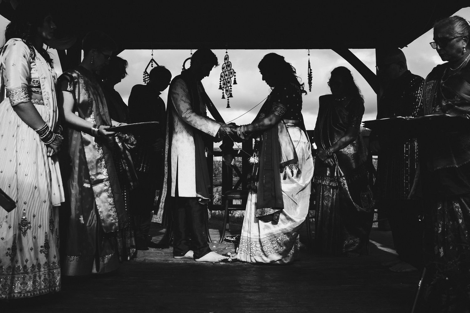 A black and white photo captures an intimate wedding ceremony moment under a rustic shelter.