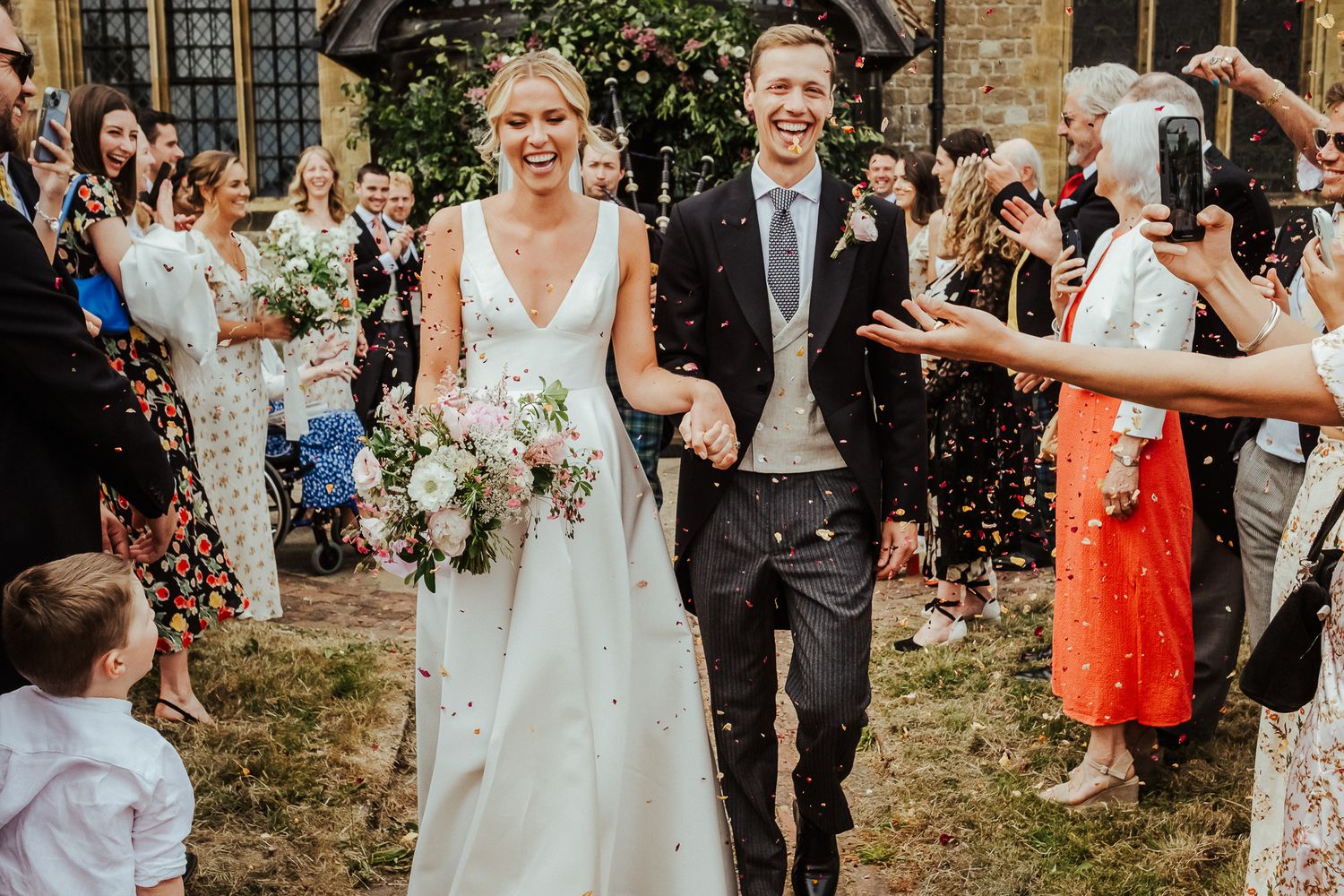 Happy couple exits church while guests throw confetti in celebration.