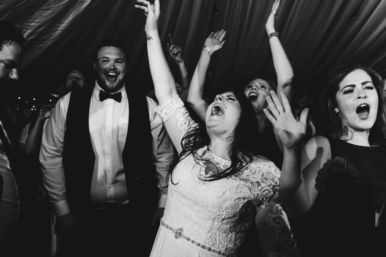 Wedding guests dancing and celebrating with joyful expressions at reception party.