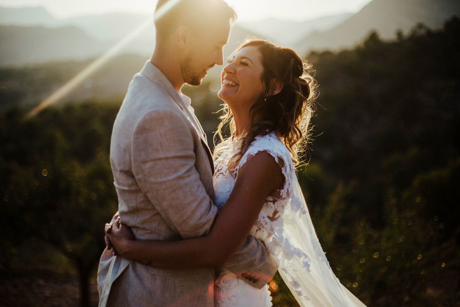 A wedding couple embraces during golden hour sunset in a scenic outdoor setting.