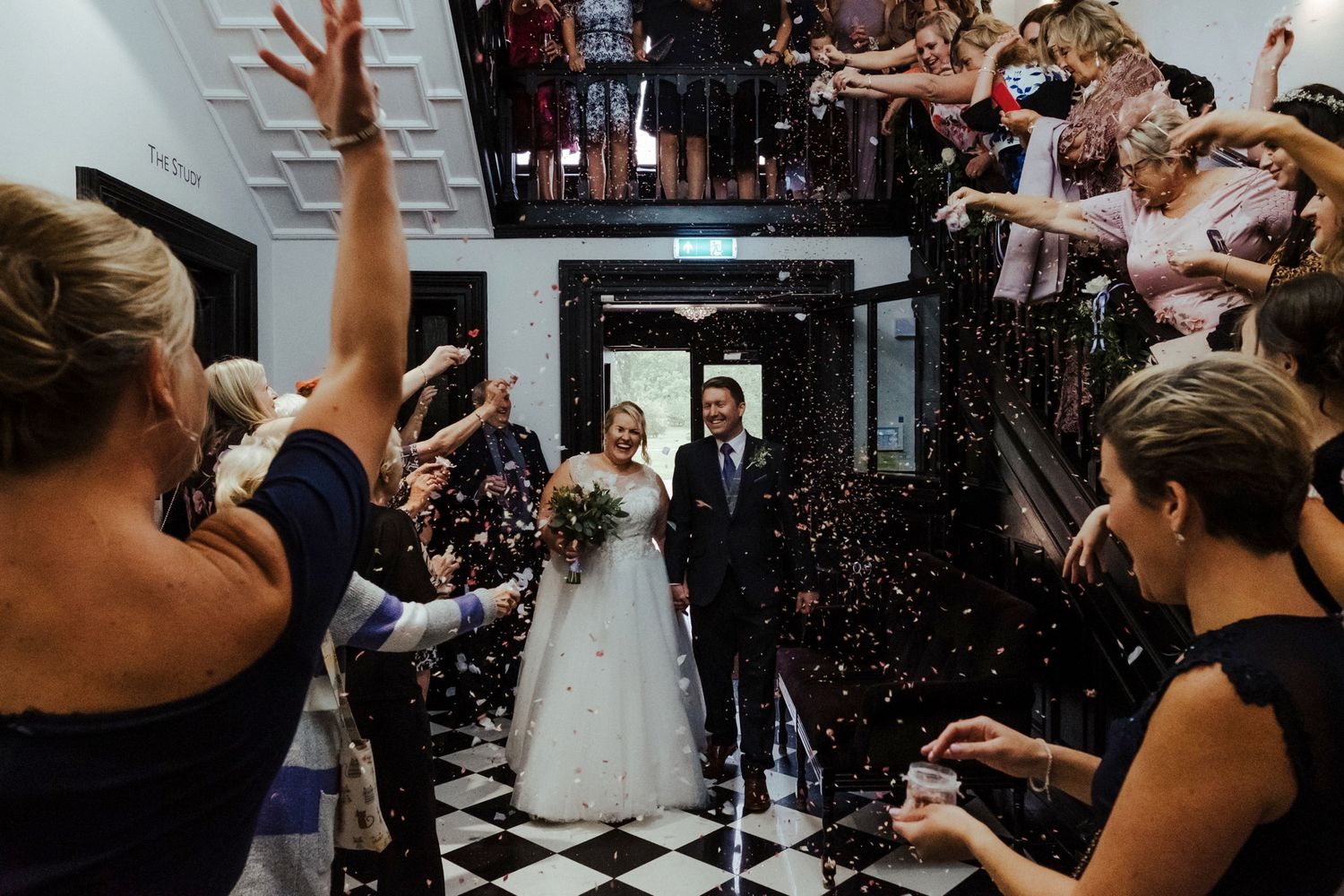 Wedding celebration with guests throwing confetti in an elegant black and white tiled venue.