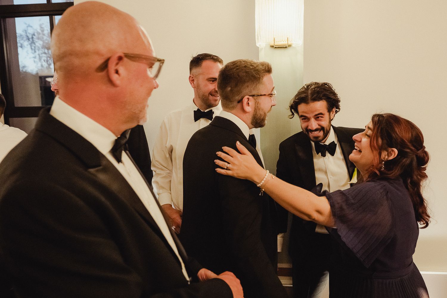 People in formal black tie attire gather and socialize at an elegant indoor event.