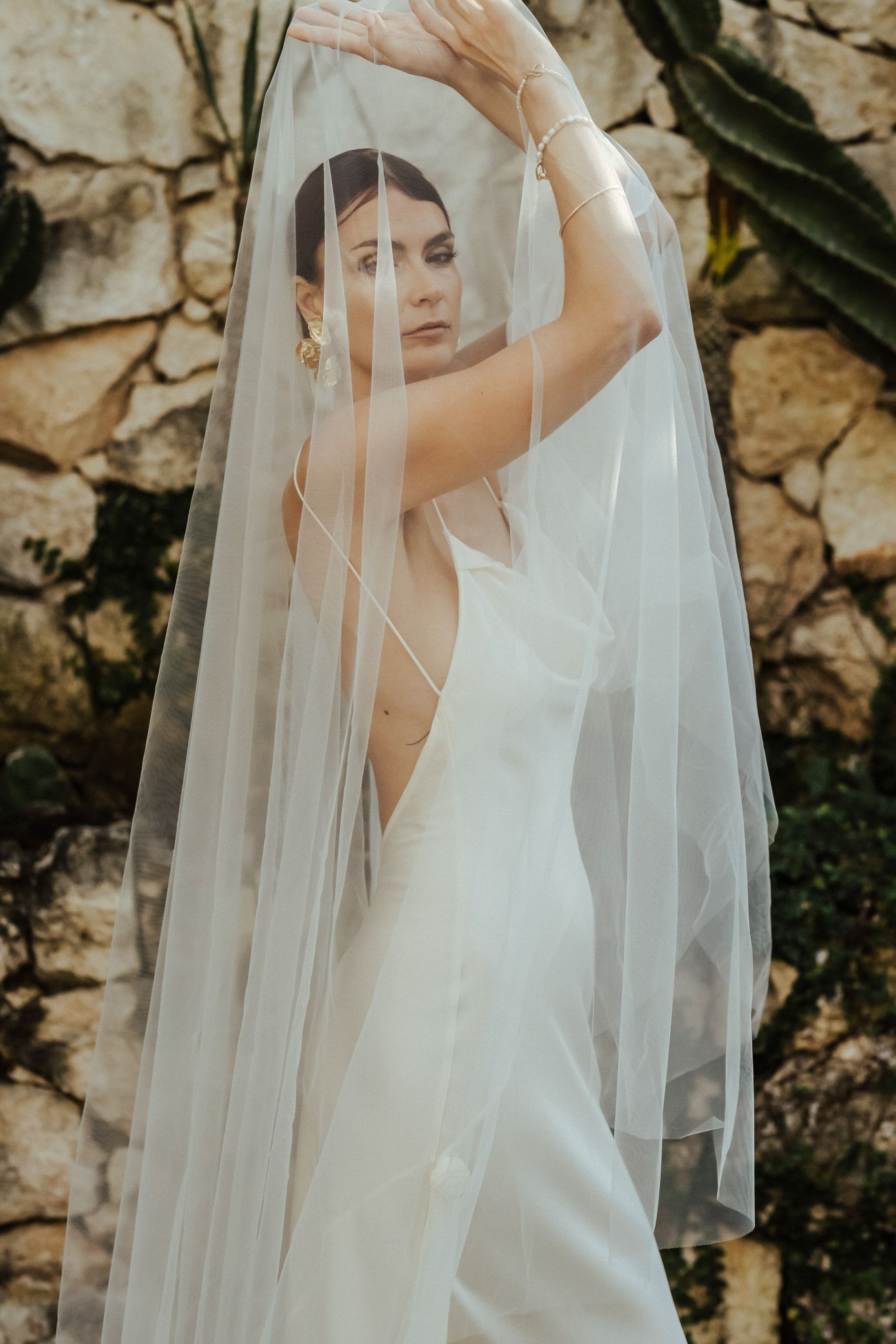 Ethereal bridal portraits featuring a flowing veil and white dress against a textured stone wall.