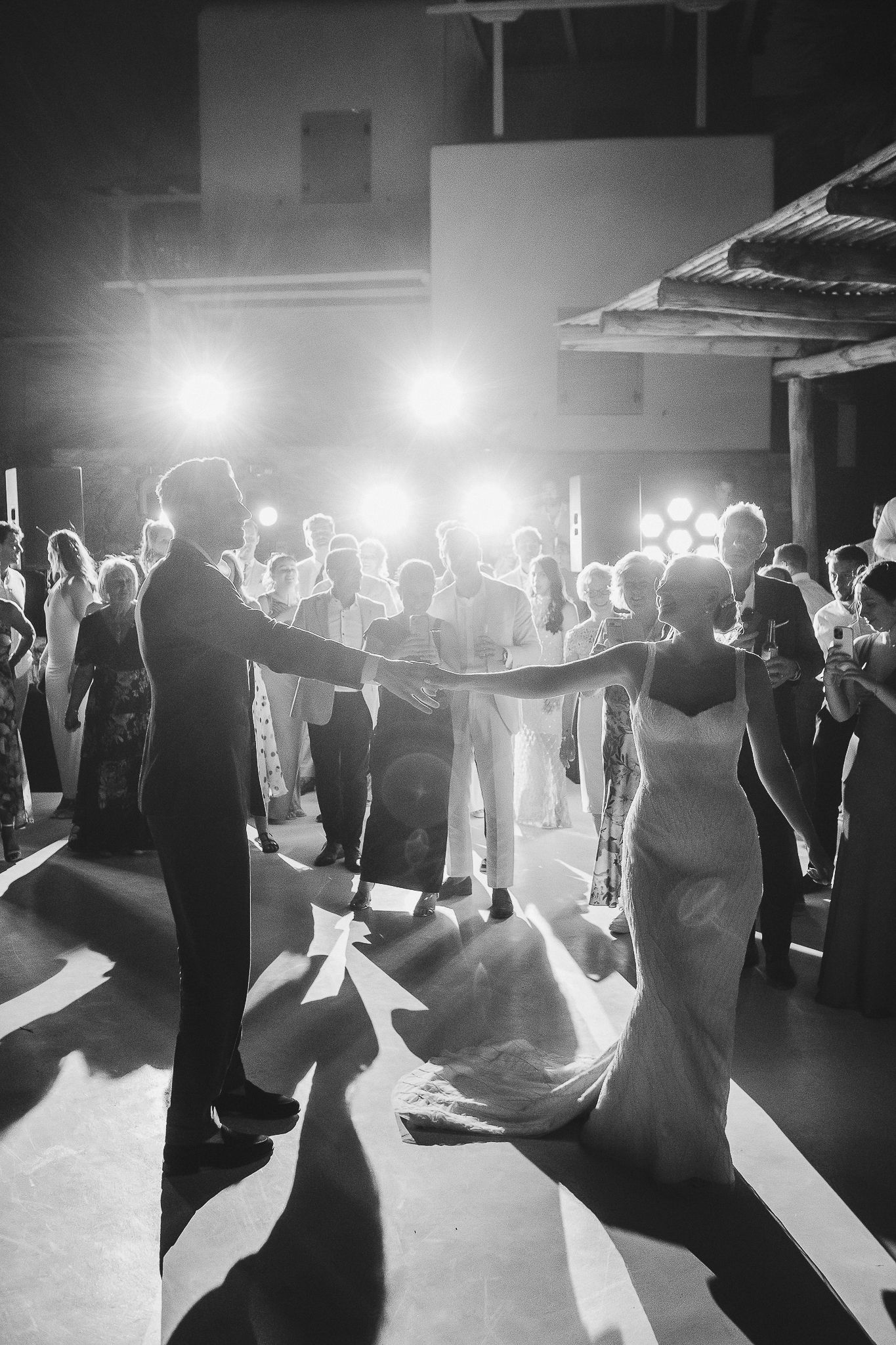 Dancing figures silhouetted on a dark dance floor with bright backlighting creating a dramatic atmosphere at an event.