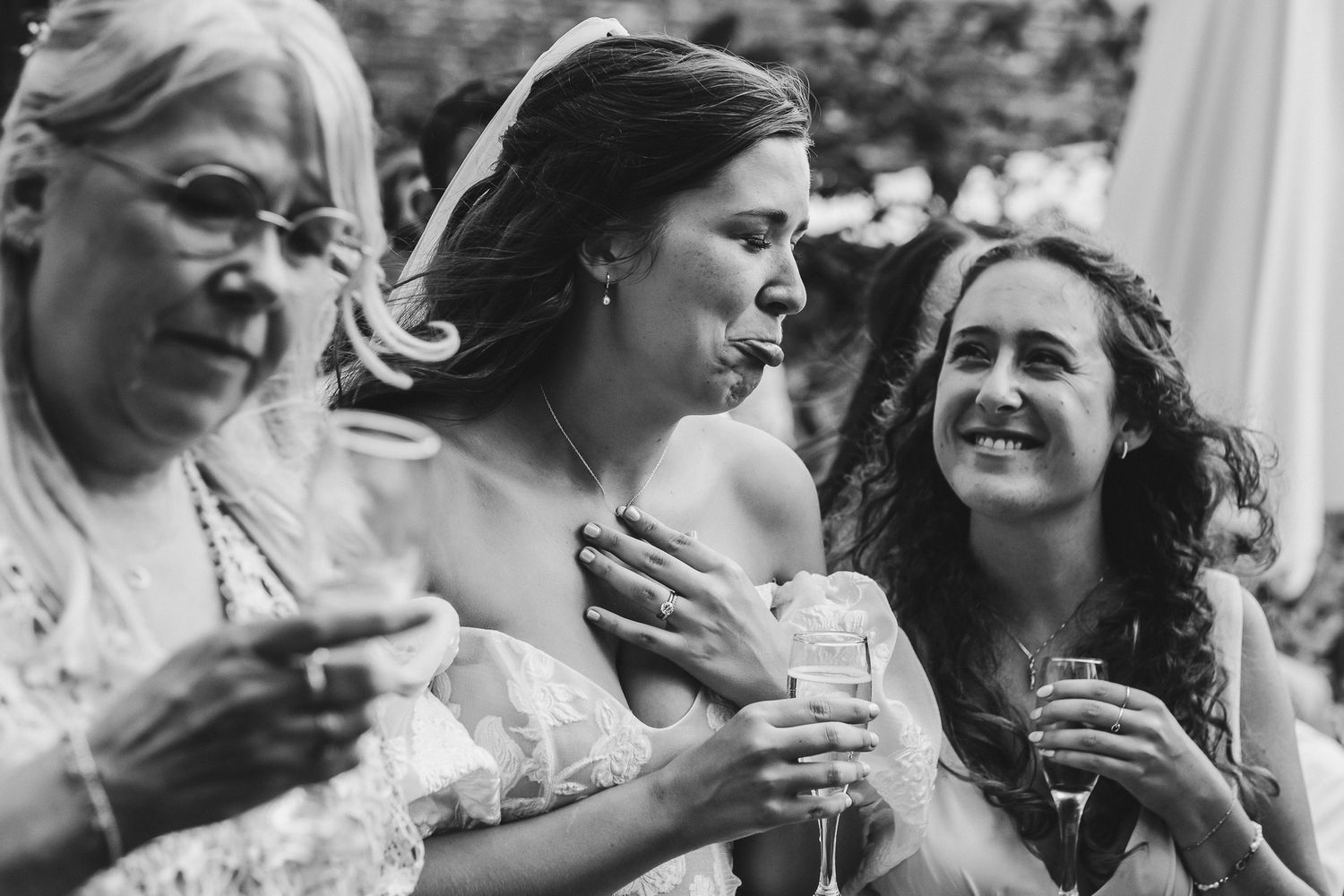 Three people laughing and enjoying drinks together at an outdoor event captured in black and white photography.