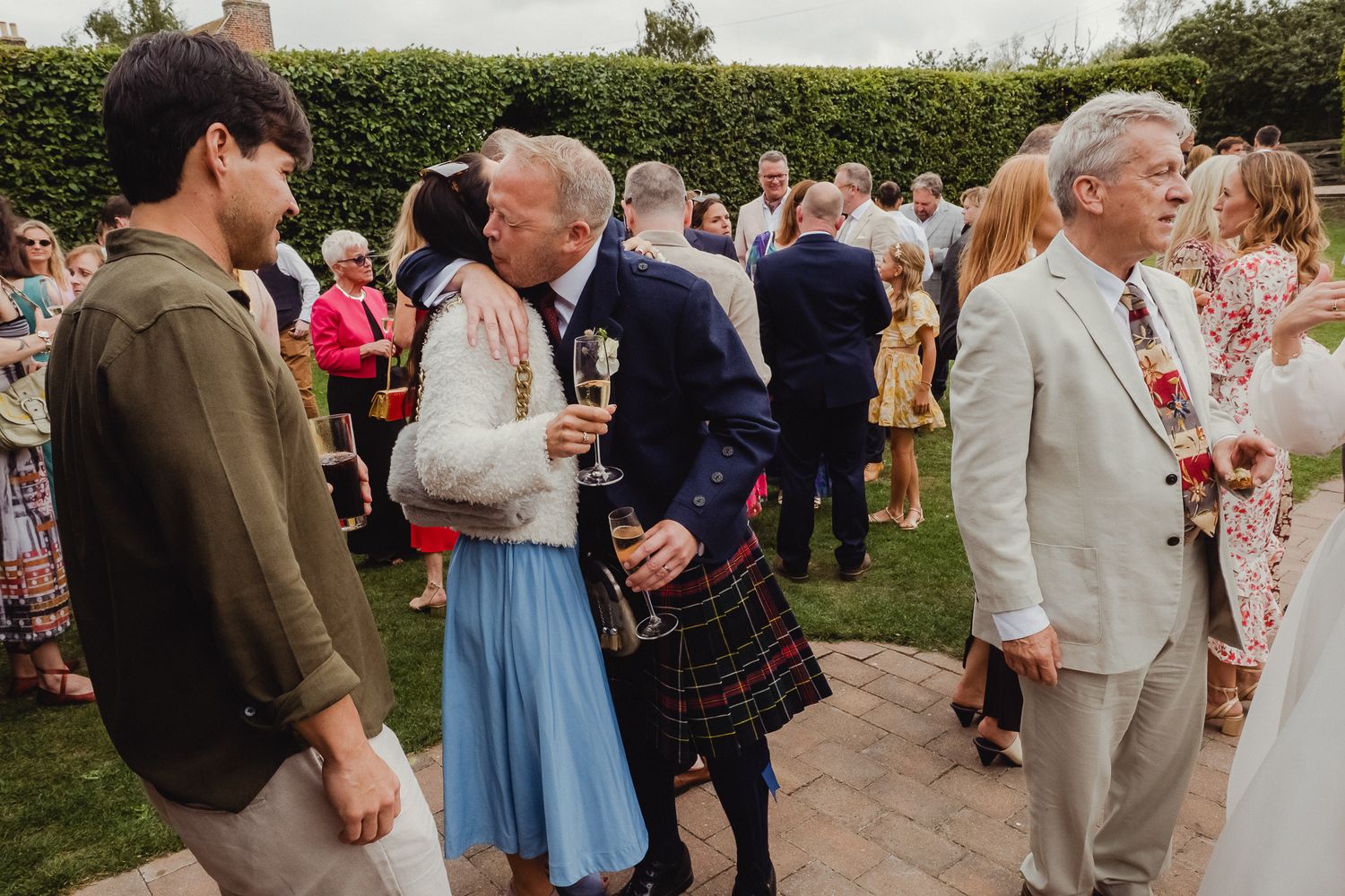 Wedding guests mingle and socialize during an outdoor garden reception on a sunny afternoon.