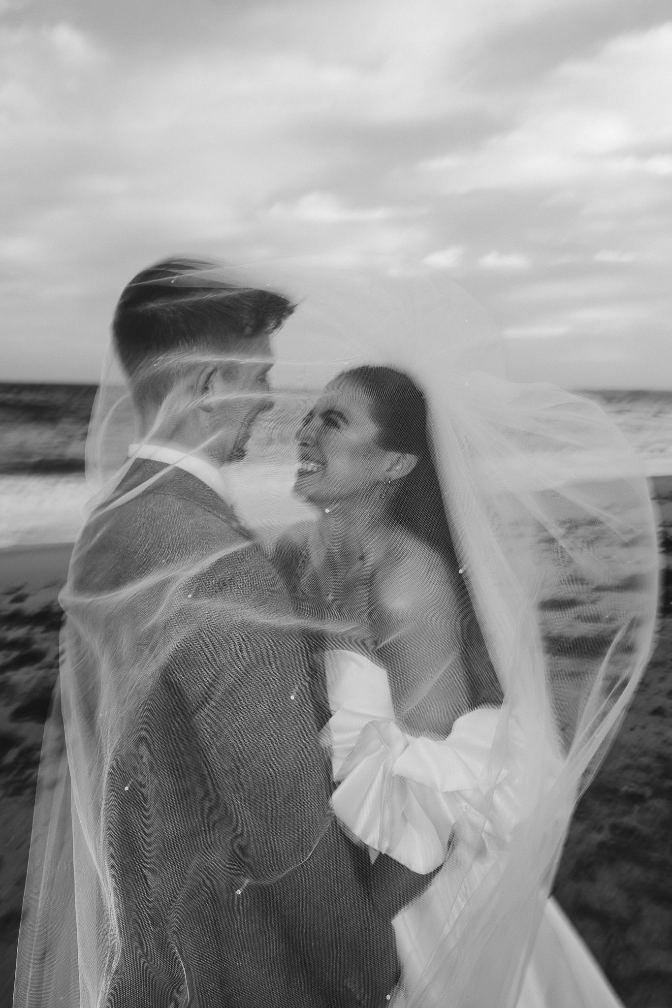 A romantic black and white wedding photo sequence shows a couple embracing as a veil flows in the wind at the beach.