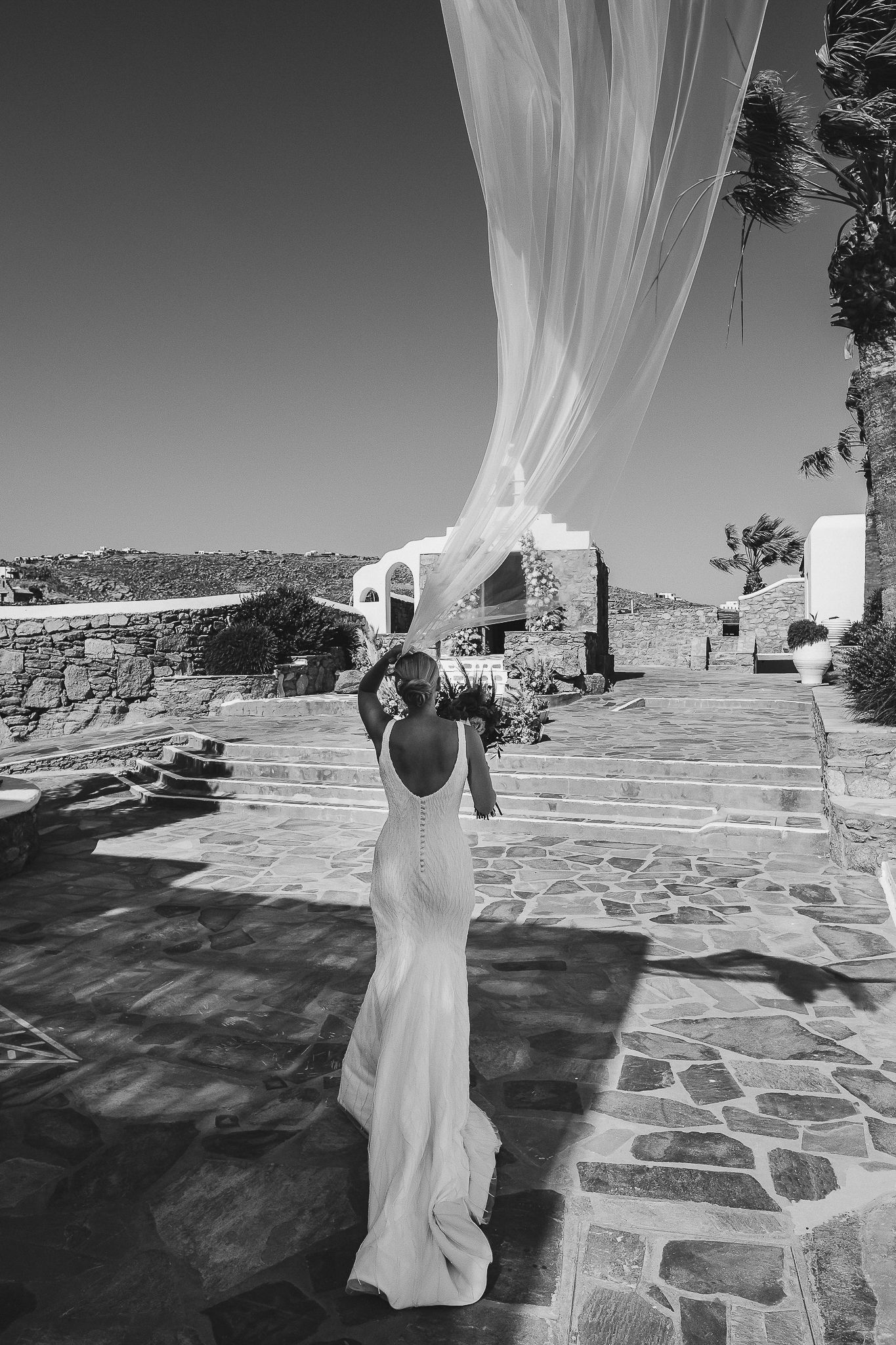 Figure in flowing white fabric dances against stone patio and blue sky in black and white photography sequence.
