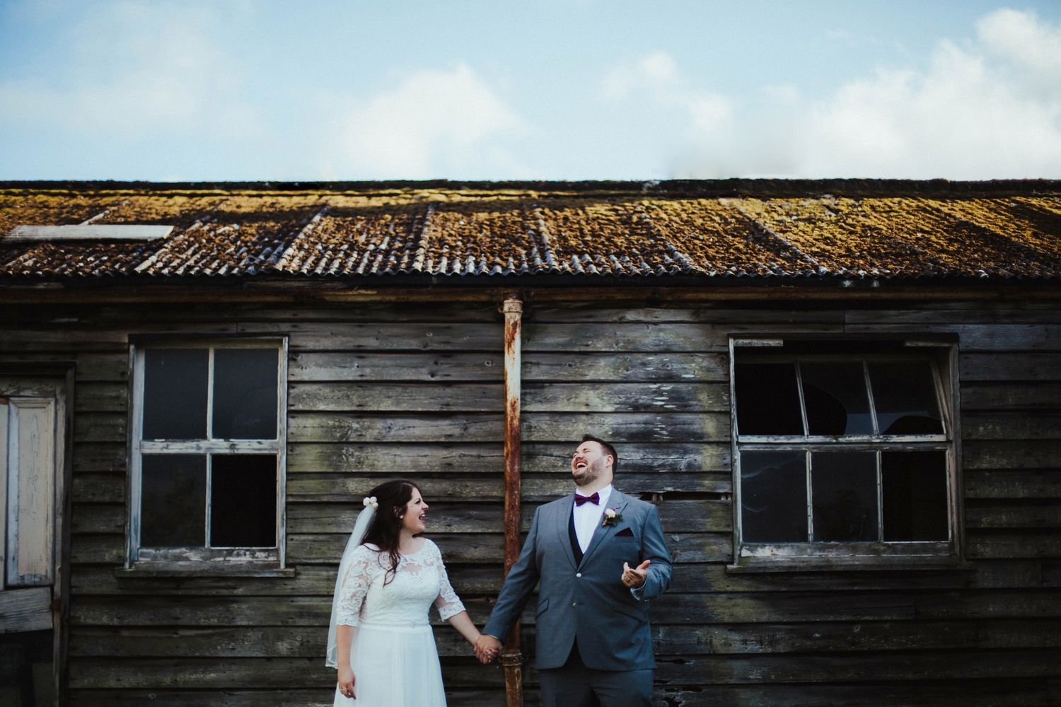 Couple poses in front of rustic wooden building with weathered siding.