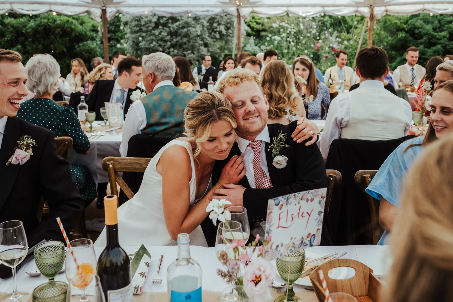 Wedding guests mingle and celebrate at outdoor reception tables under string lights.