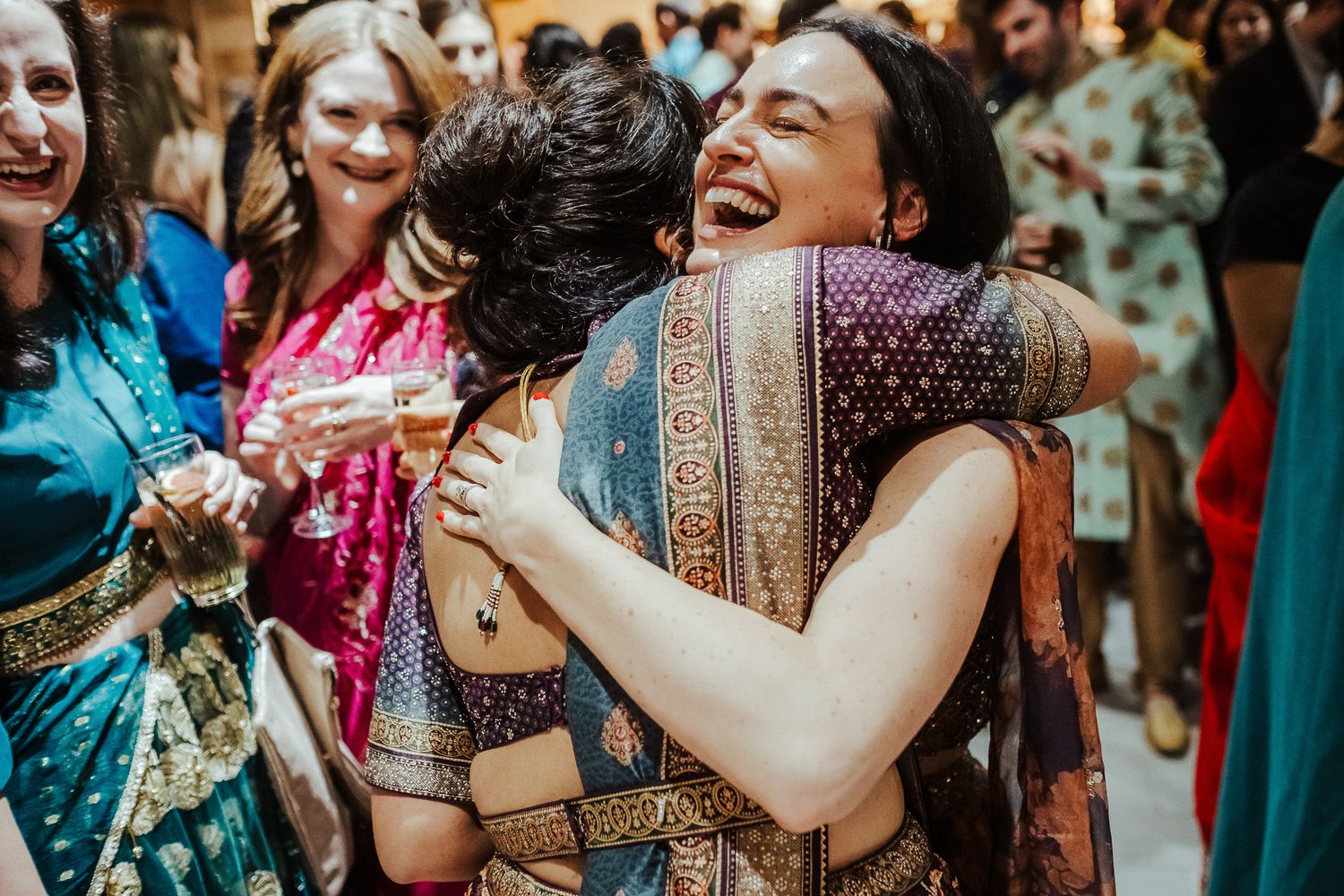 Two people sharing a joyful embrace at a colorful Indian wedding celebration.
