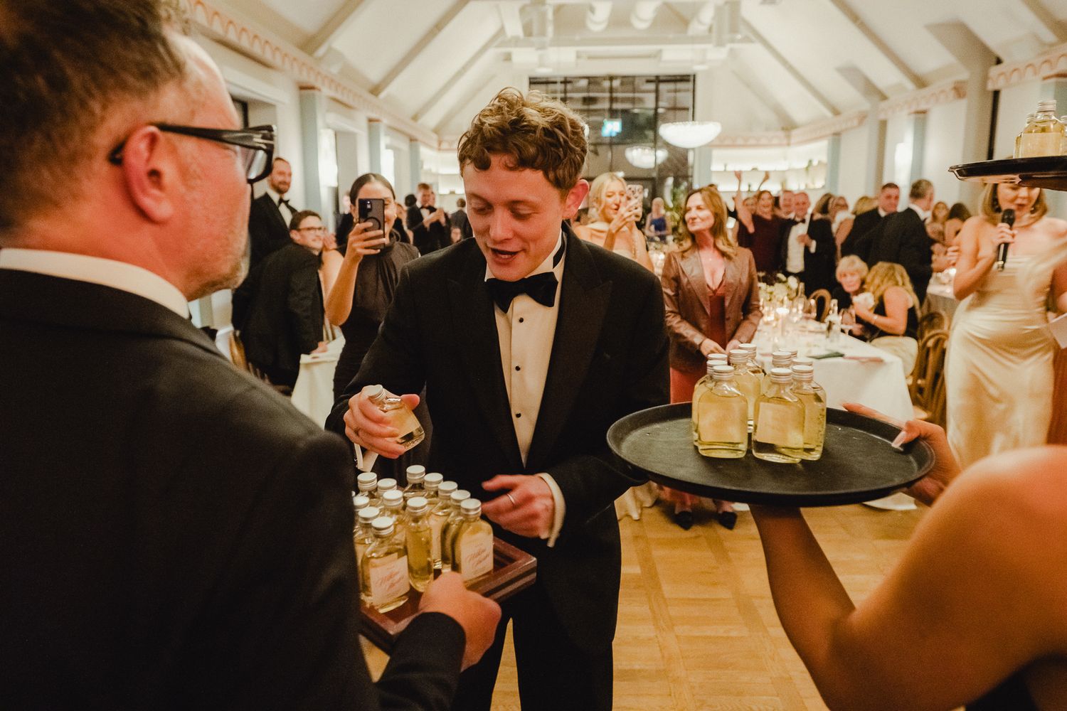 Guests enjoying drinks and conversation during an elegant wedding reception in a bright, ornate ballroom.