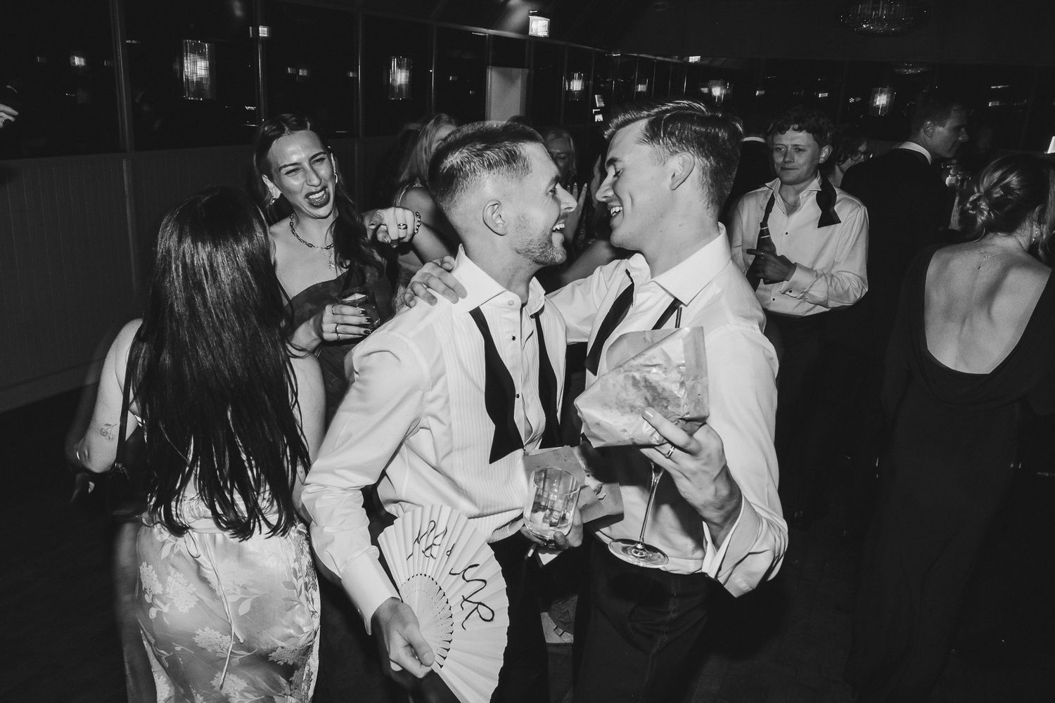 Black and white photo of people socializing and dancing at a lively party or nightclub.