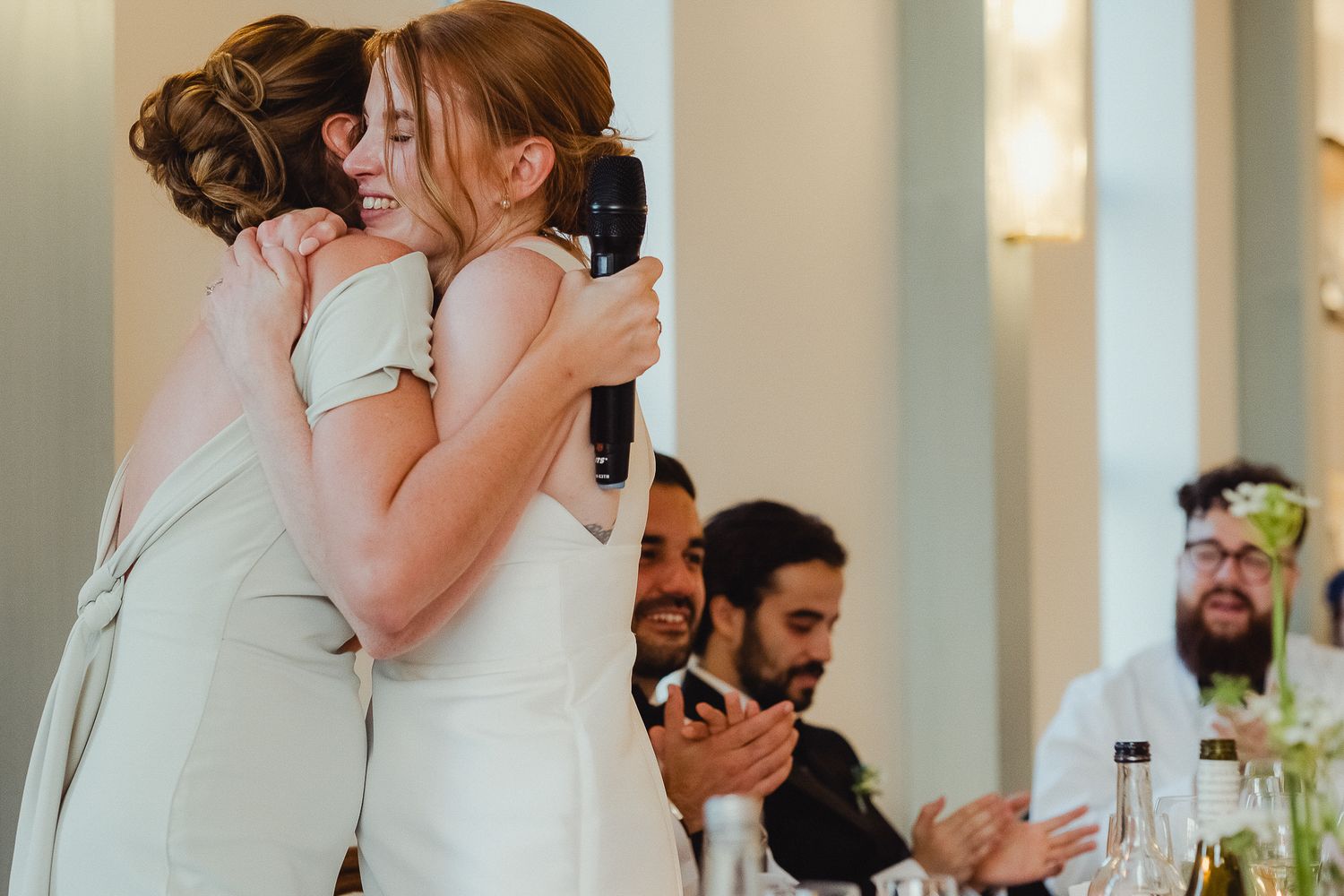 Guests celebrate at an elegant indoor wedding reception with white columns and soft lighting.