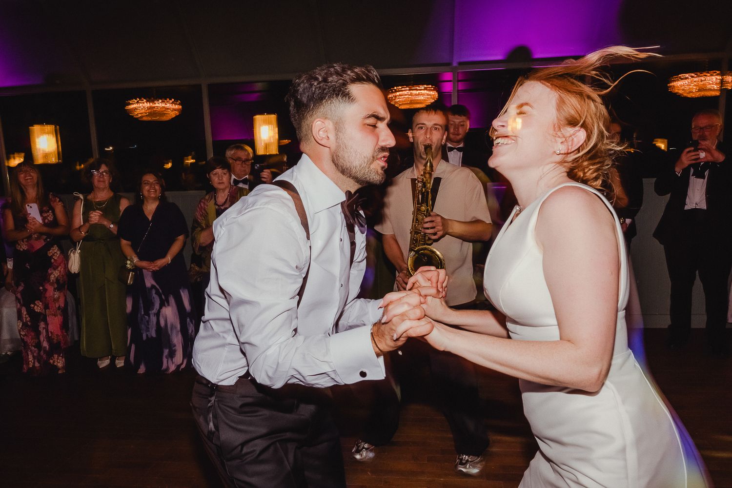 Couples dance together during a reception celebration in a dimly lit venue with purple lighting effects.