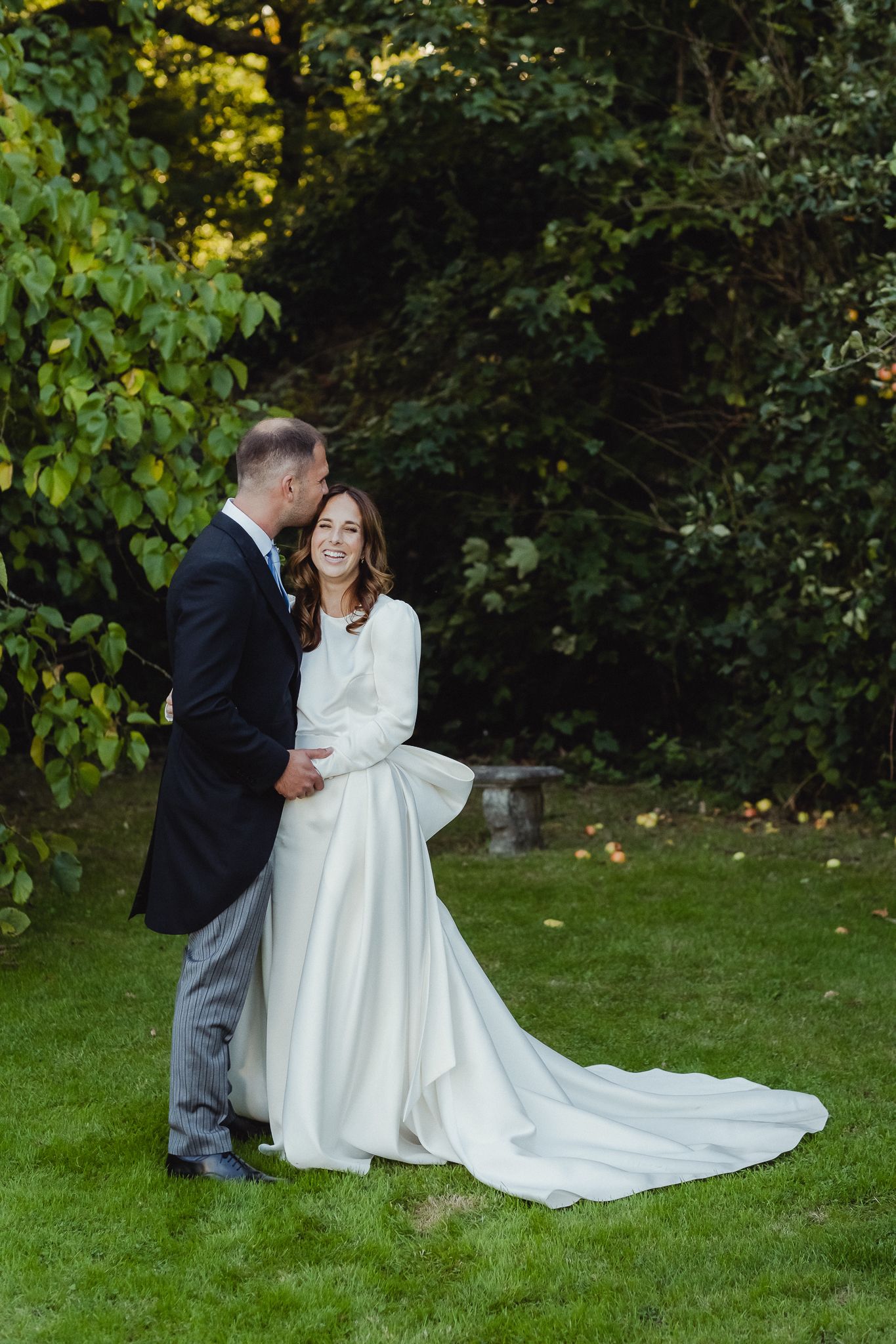 A couple shares an intimate moment in a garden setting, with the bride wearing a flowing white gown with long train.