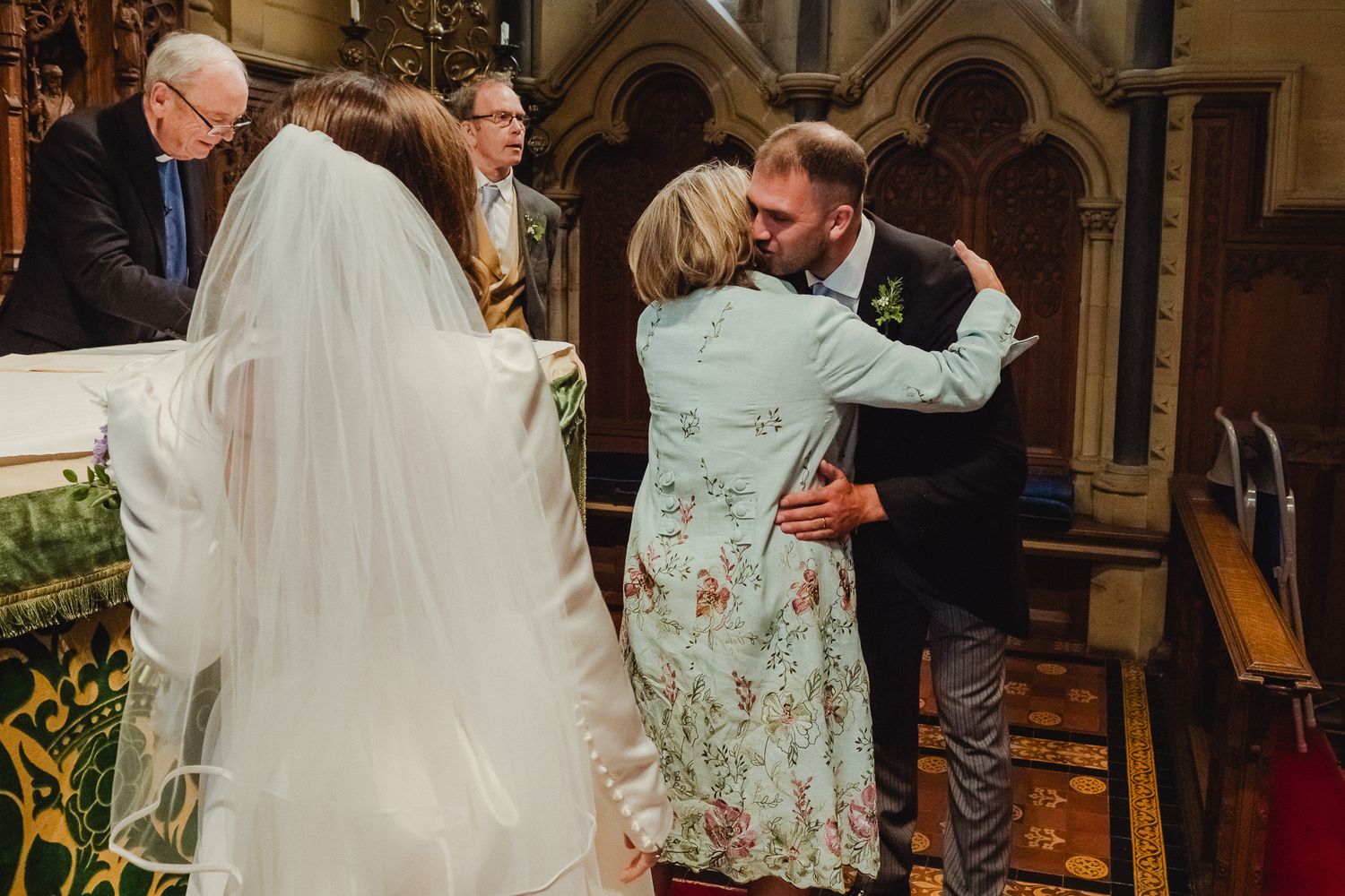 Wedding party celebrates with joyful dancing and embraces in an elegant venue with arched architecture.