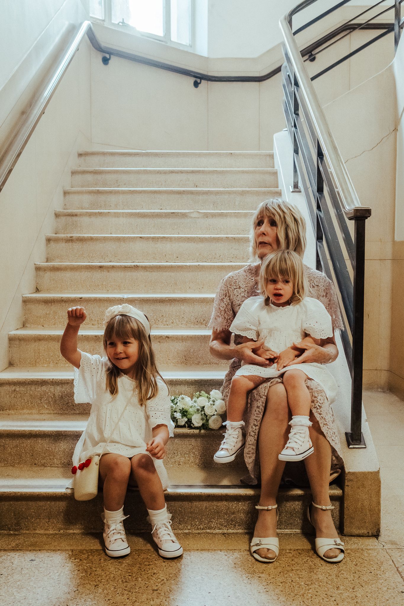 Three figures sitting on stone stairs indoors with natural lighting and white walls.