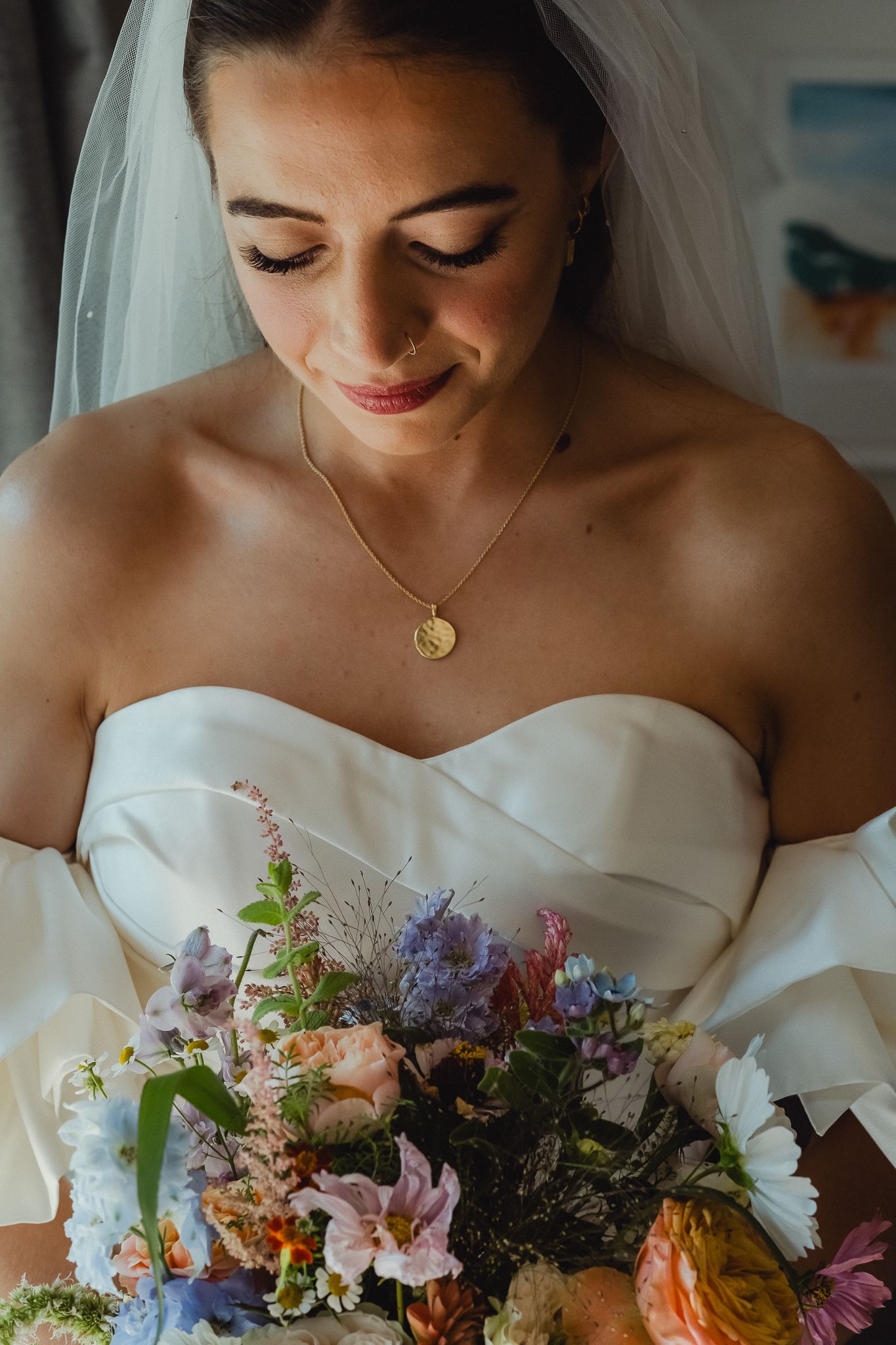 Close-up of bride in white strapless gown looking down at colorful wildflower wedding bouquet.