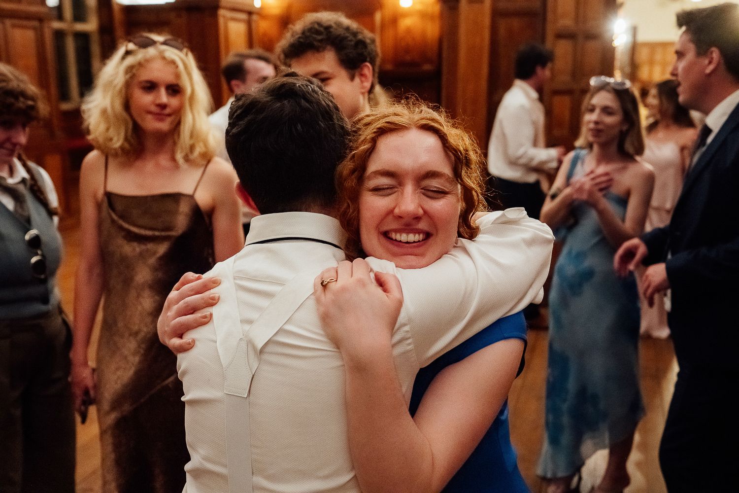 Joyful woman in blue dress hugging a man on a wedding dance floor surrounded by guests.