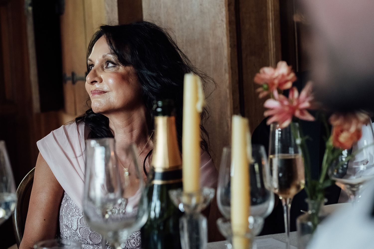 Elegant woman at a wedding reception table with champagne glasses, candles, and floral centerpieces in warm ambient light.