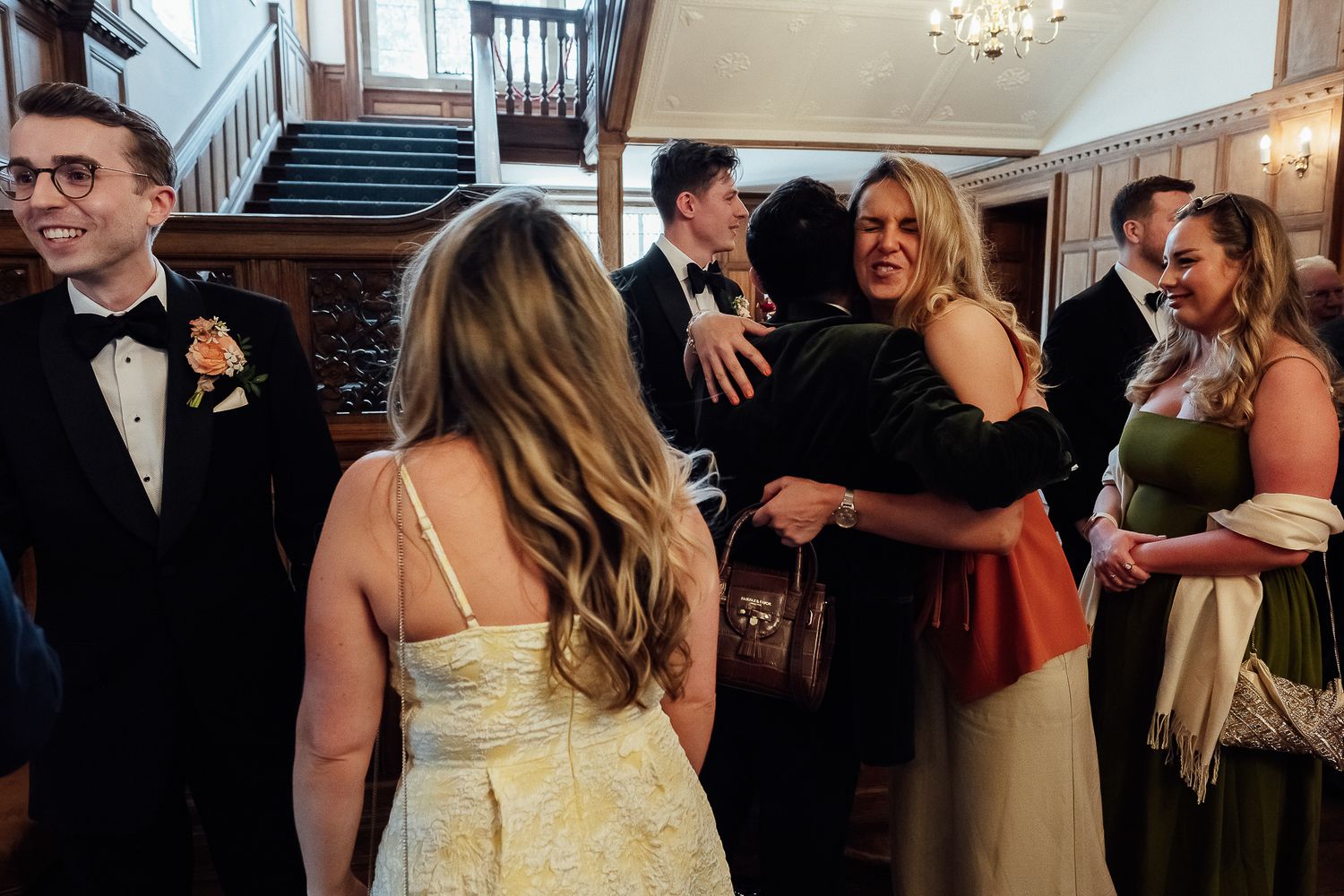 Guests hugging and socializing at a formal wedding reception in an elegant venue with wood paneling.