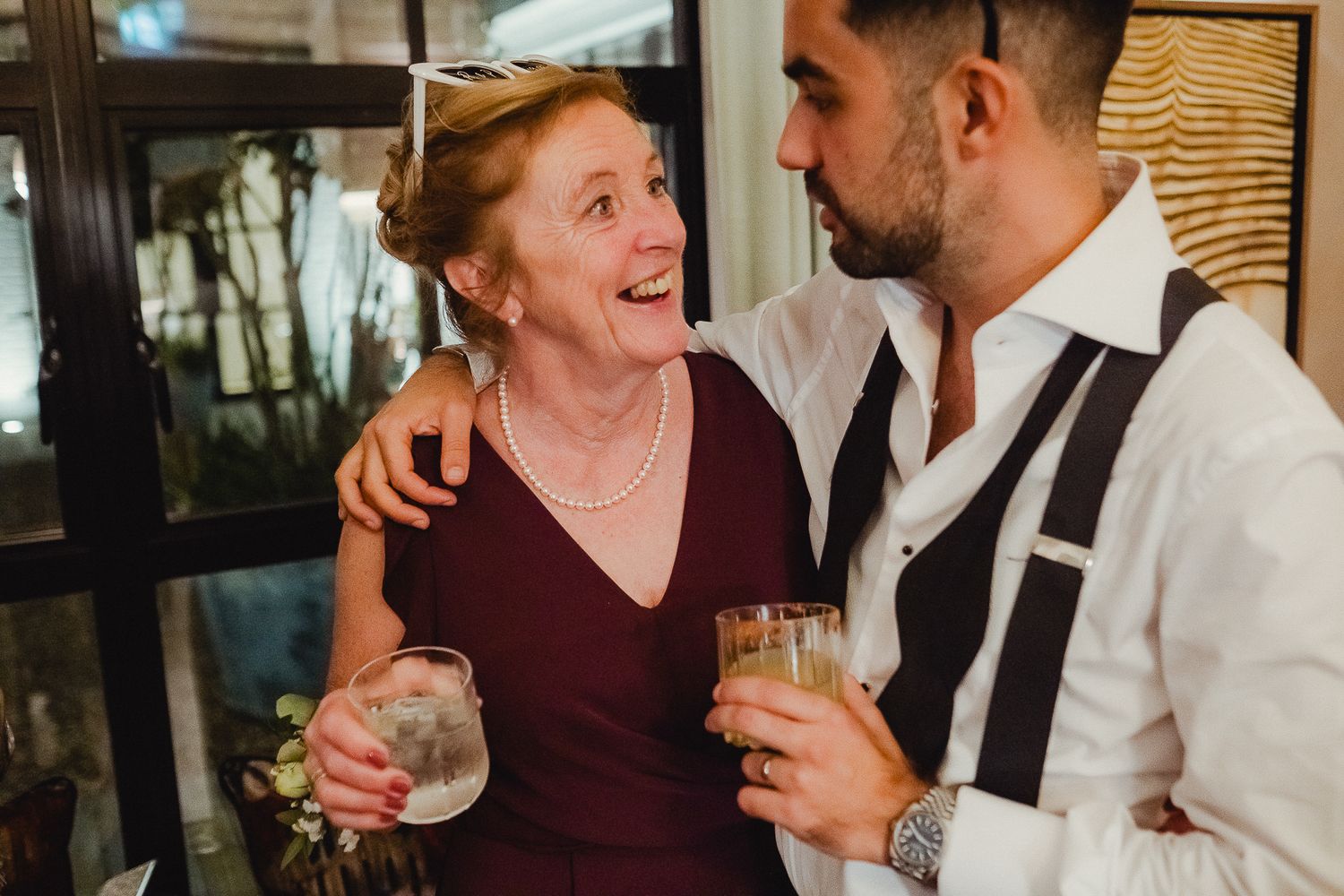 Two people share a laugh while holding drinks at a social gathering in an elegant indoor setting.