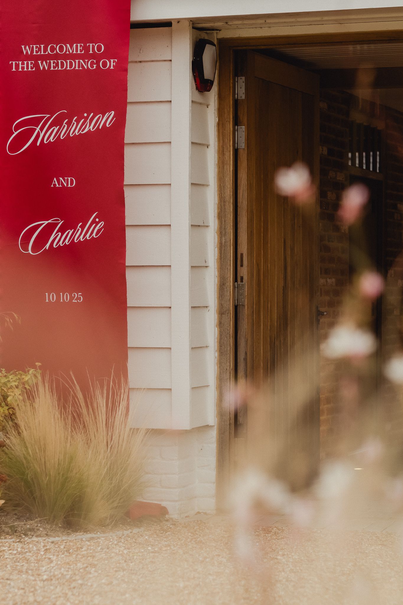 Modern wedding welcome sign in burgundy red with elegant script text displayed outside a white building entrance.