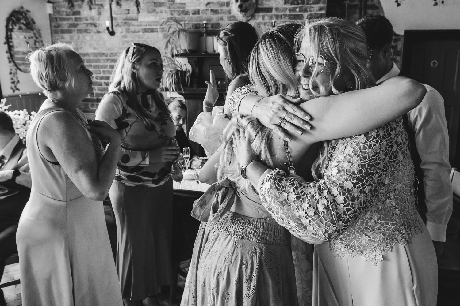 Wedding guests dance and celebrate together on a rustic brick-walled dance floor in black and white.