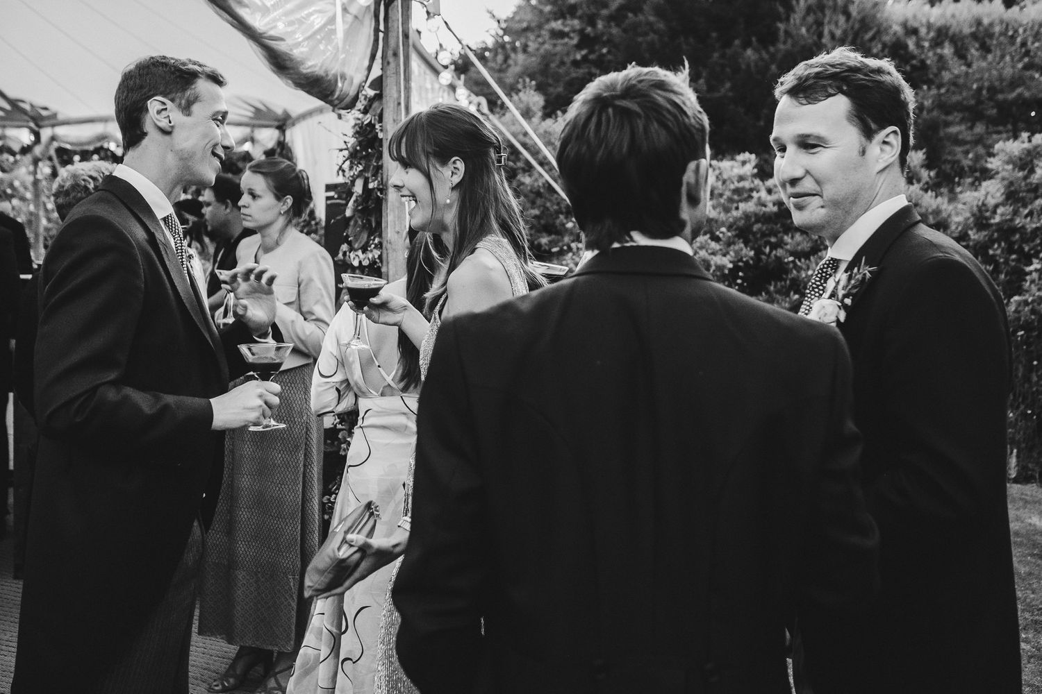 Wedding guests gather for cocktail hour conversations at an outdoor garden reception.