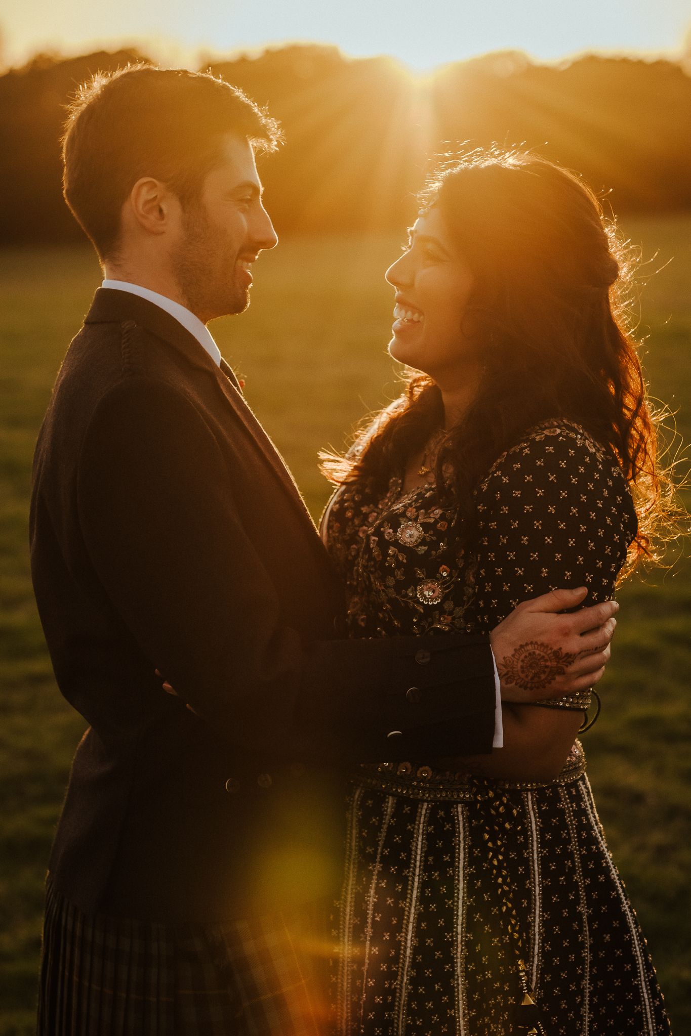 Couple in traditional Scottish and Indian attire sharing an intimate moment at golden hour.