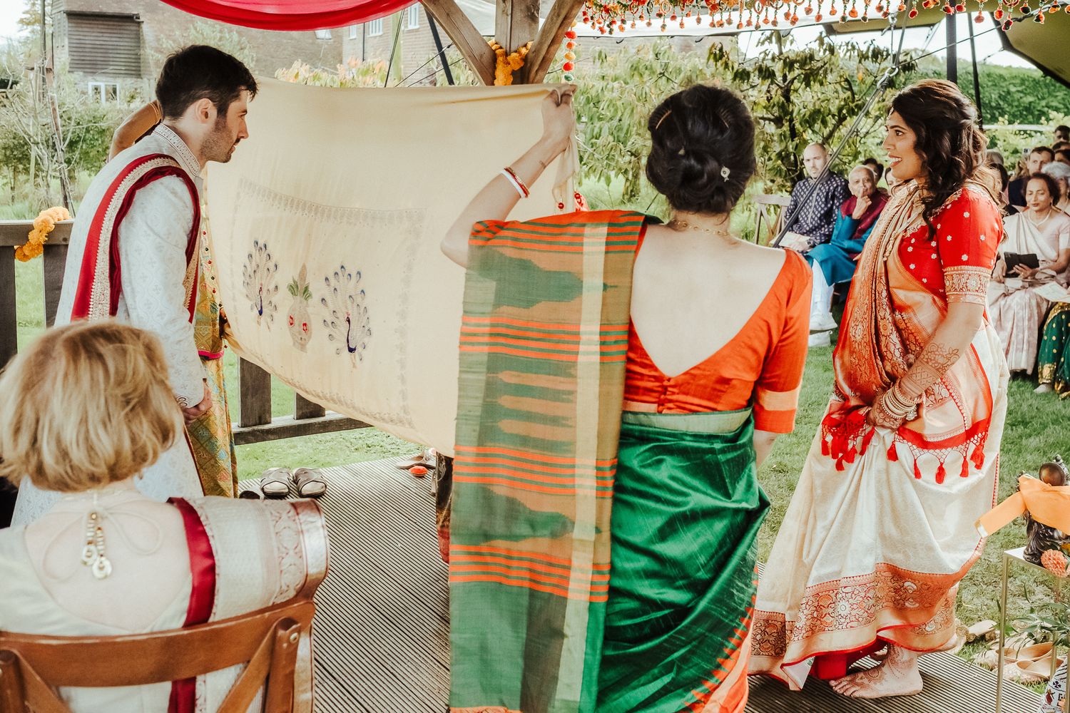 People in traditional attire participating in a cultural wedding ceremony under a canopy.