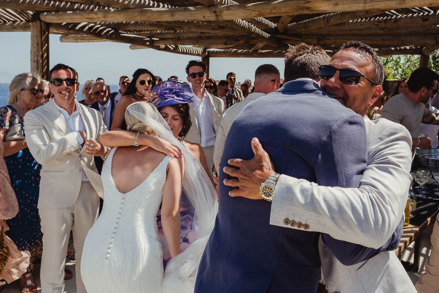 Wedding guests dancing together under a rustic wooden pergola during an outdoor celebration.