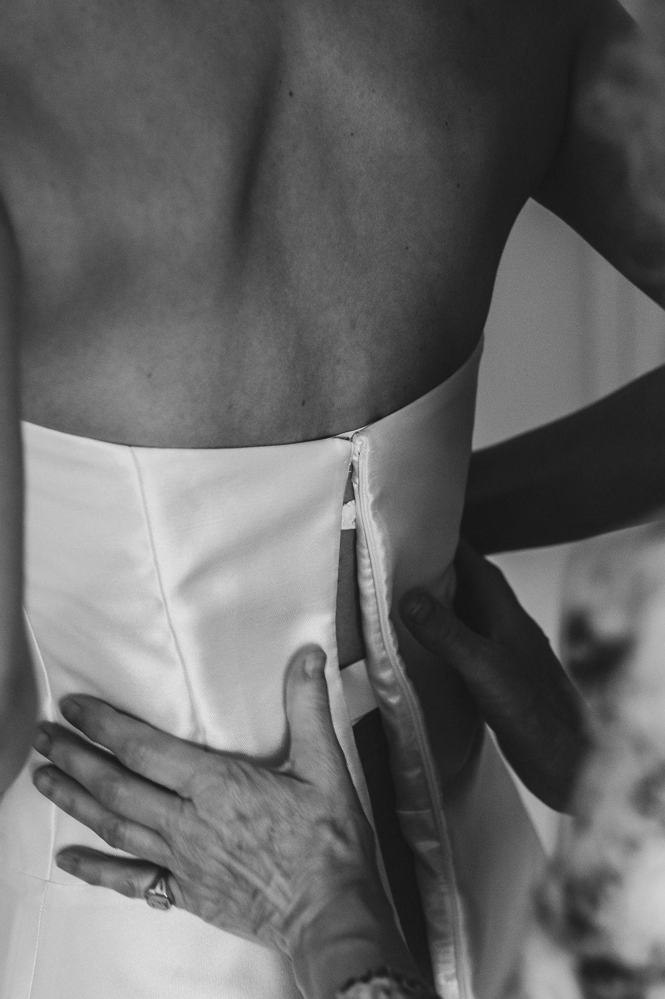 Black and white photo showing someone adjusting a white collar or neckline against a dark background.