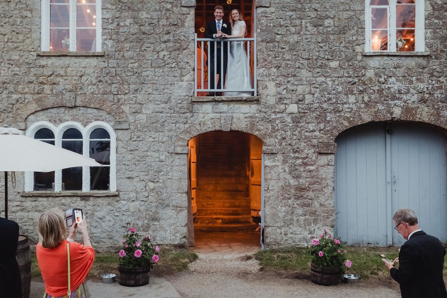 Wedding guests celebrate and gather outside a rustic stone building with glowing windows at dusk.