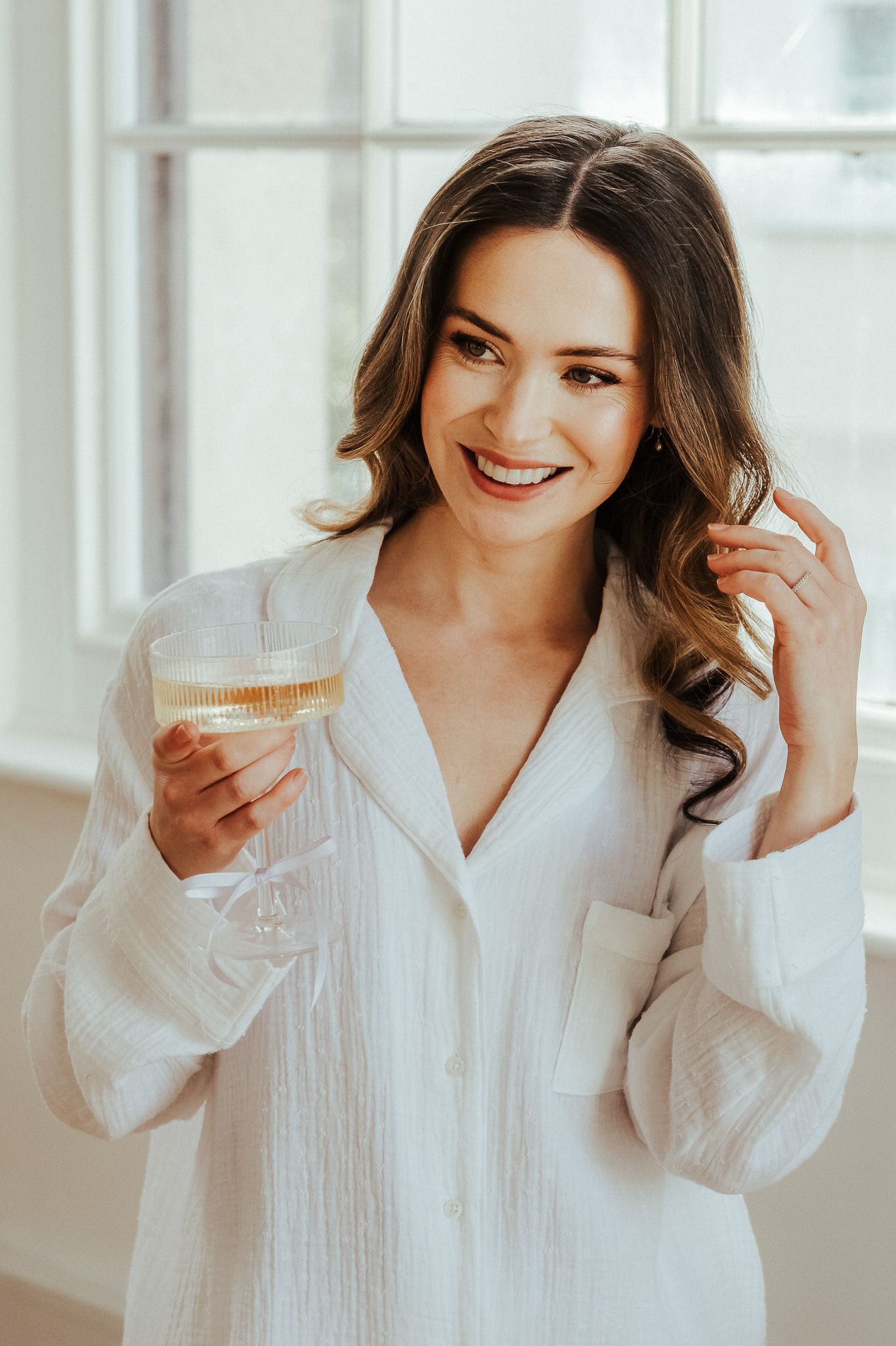 Woman in white button-down shirt smiles and poses in bright indoor setting with natural lighting.