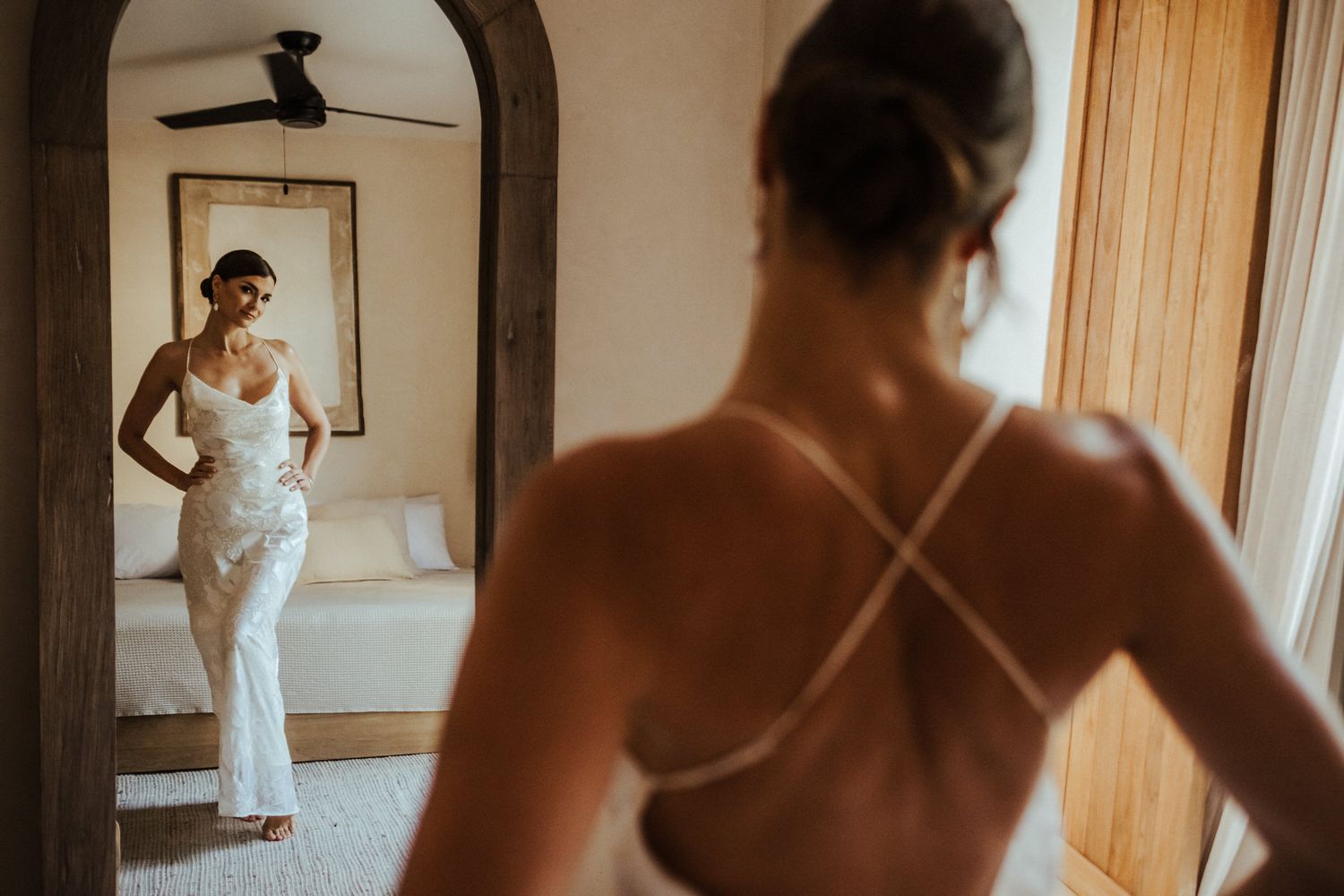 A person in a white wedding dress looks at their reflection in a mirror while getting ready for their special day.