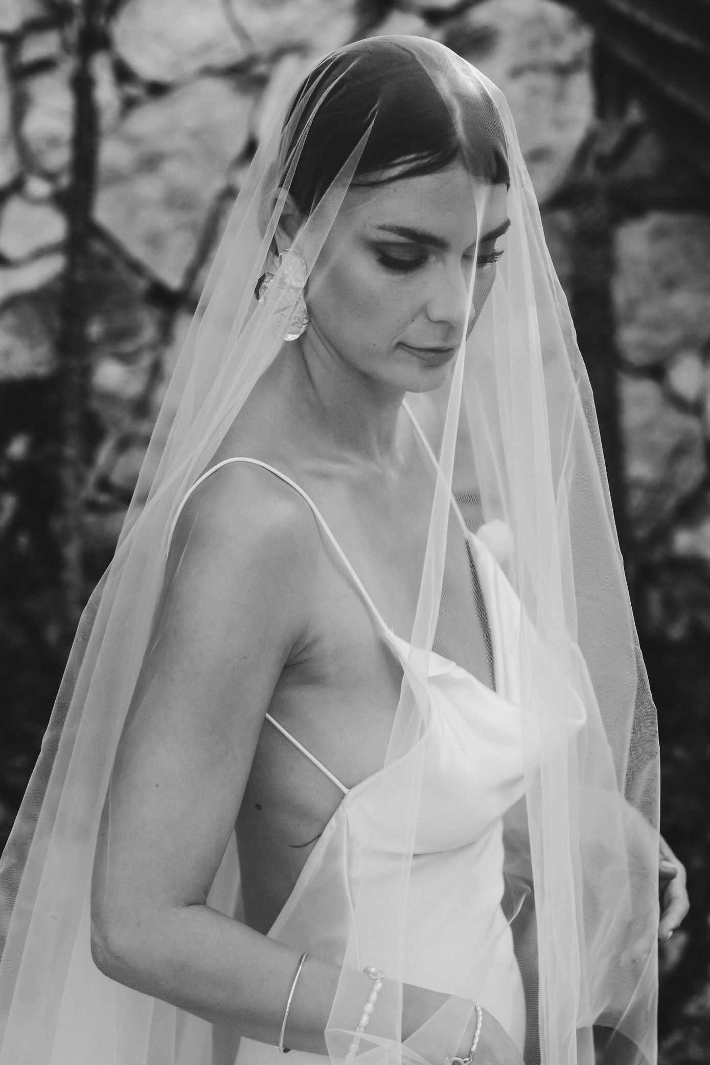 A bride in a white wedding dress and flowing veil looks down in a series of black and white portrait photographs.