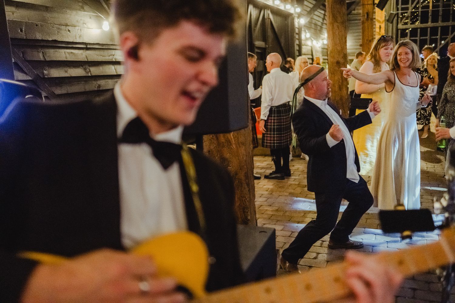 Wedding guests dancing and celebrating on a dimly lit dance floor during an evening reception celebration.