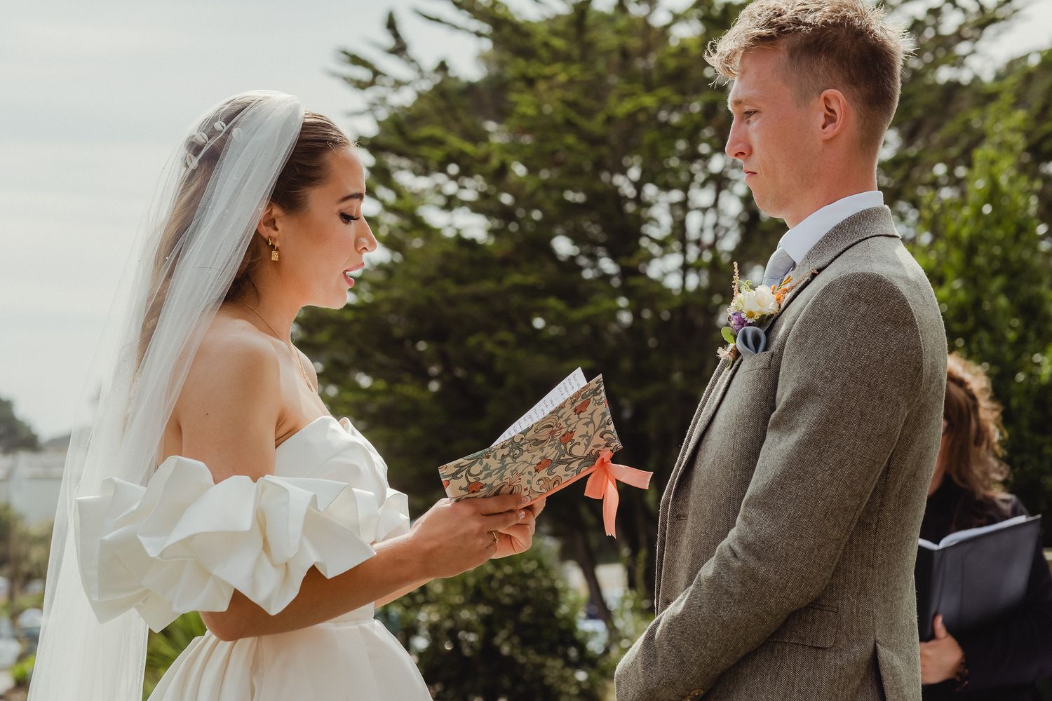 A bride and groom share a romantic moment during their outdoor wedding ceremony surrounded by lush greenery.