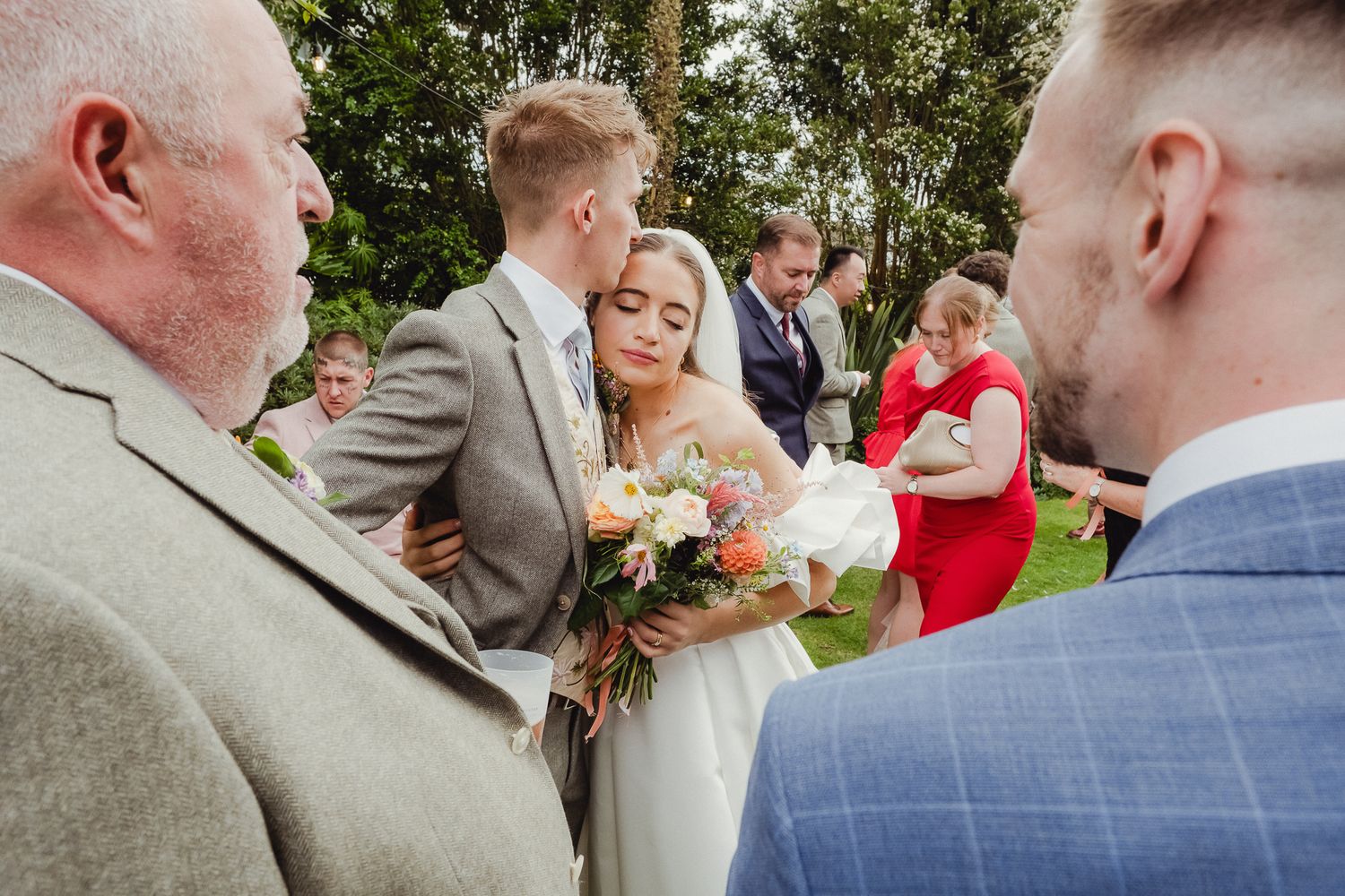 Wedding party members share hugs and greetings during an outdoor celebration.