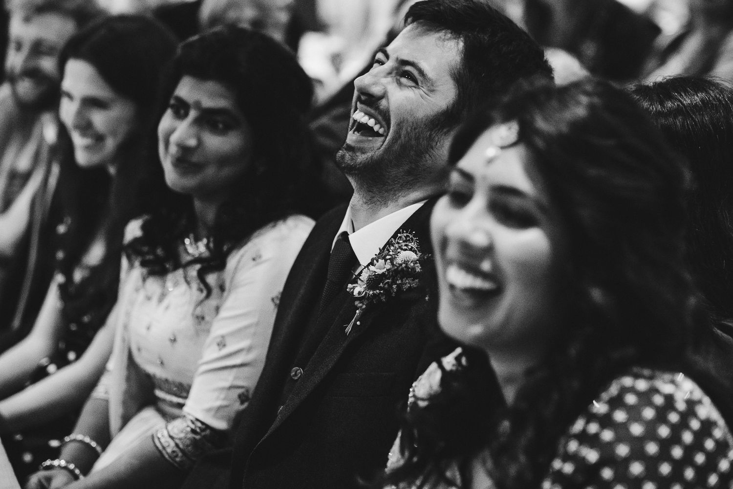 Wedding guests laugh together during a candid black and white moment.