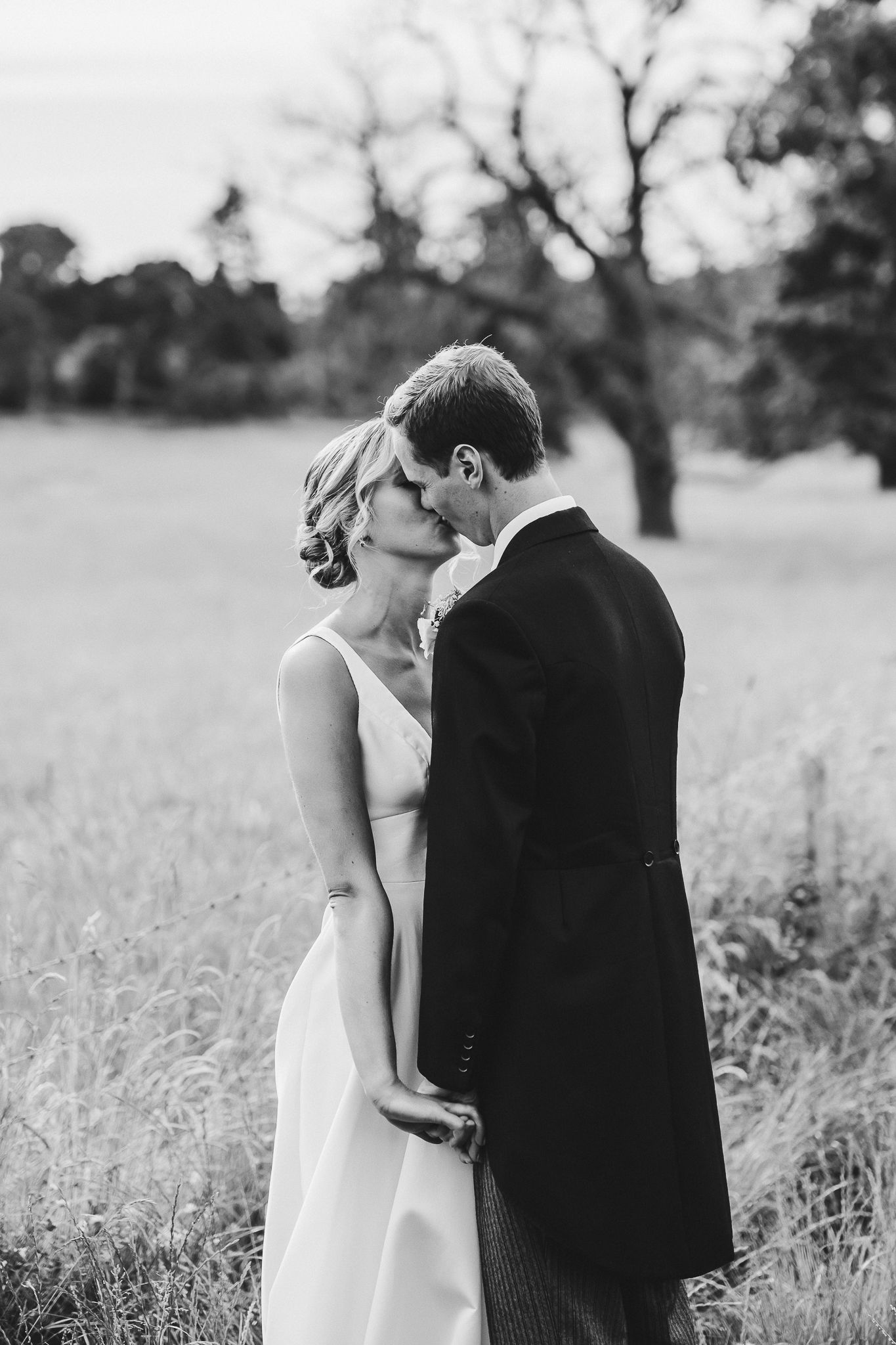 A romantic black and white portrait of a couple embracing in a meadow on their wedding day.