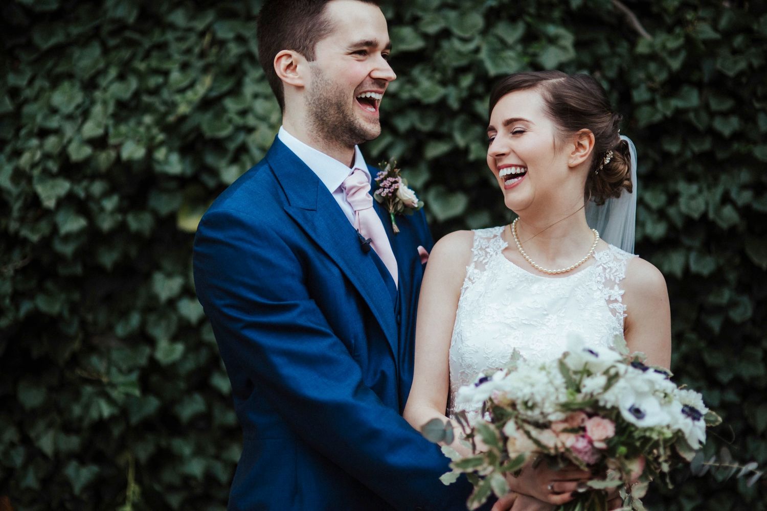 Happy couple sharing joyful moment against ivy-covered wall background.
