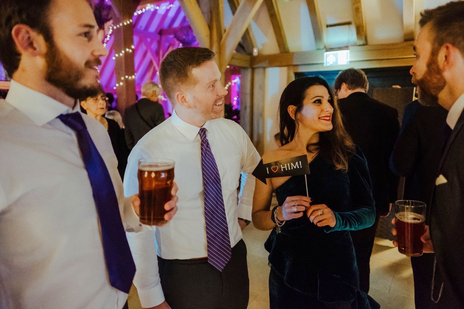 Wedding guests enjoying drinks and conversation at an indoor reception with purple ambient lighting.