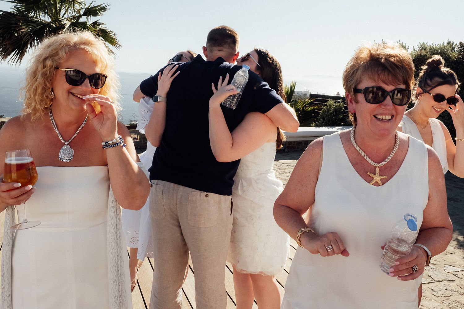 Group of women in white outfits celebrating at an outdoor party, with a couple embracing in the background.