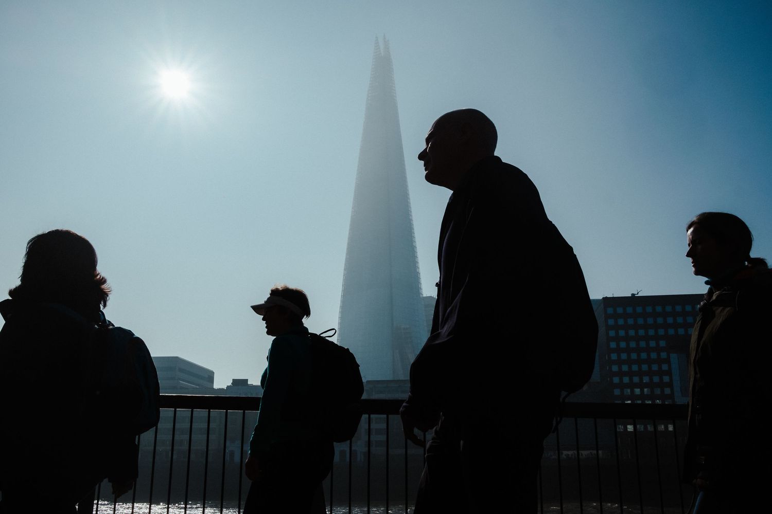 Silhouettes of people walking against a bright sky with buildings and the Shard tower visible in London.