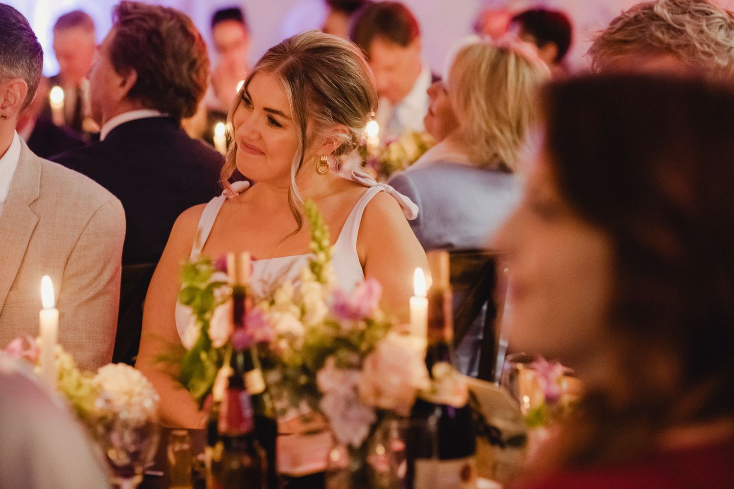 Guests enjoy an intimate candlelit dinner reception at an elegant wedding celebration with warm ambient lighting.