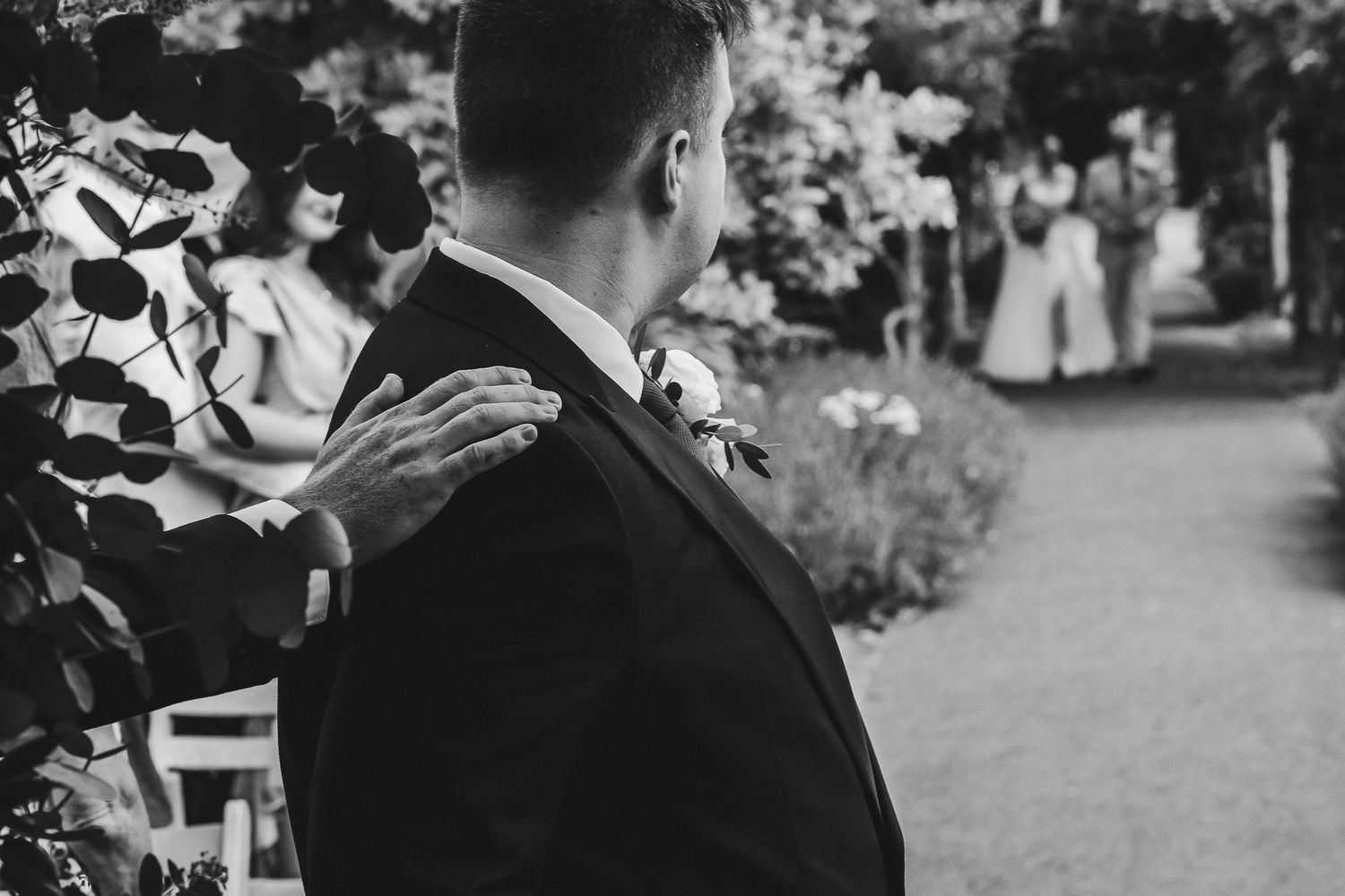 Black and white photo of a wedding couple dancing outdoors surrounded by guests at a garden reception.